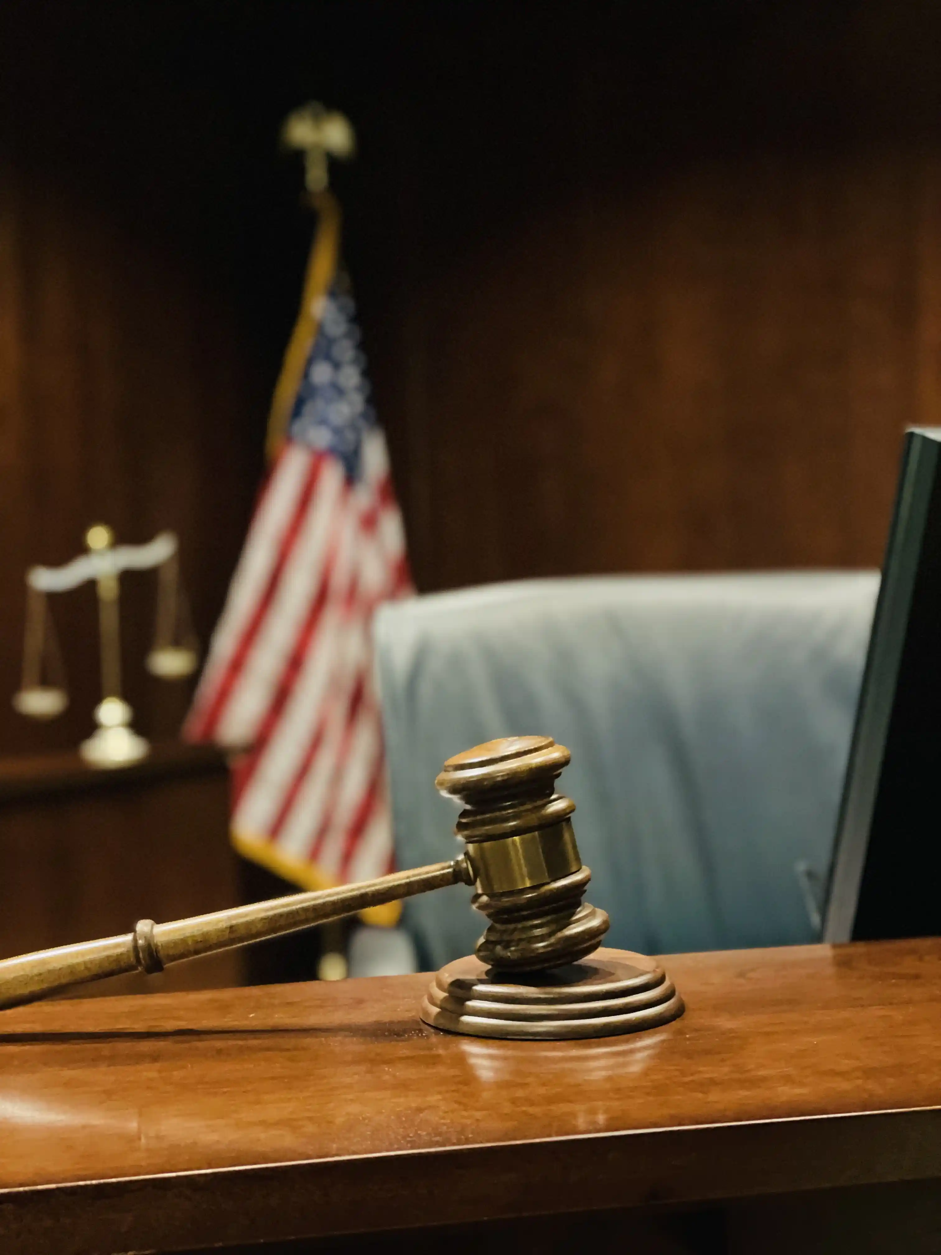A judge's gavel on a courtroom bench with an American flag and scales of justice