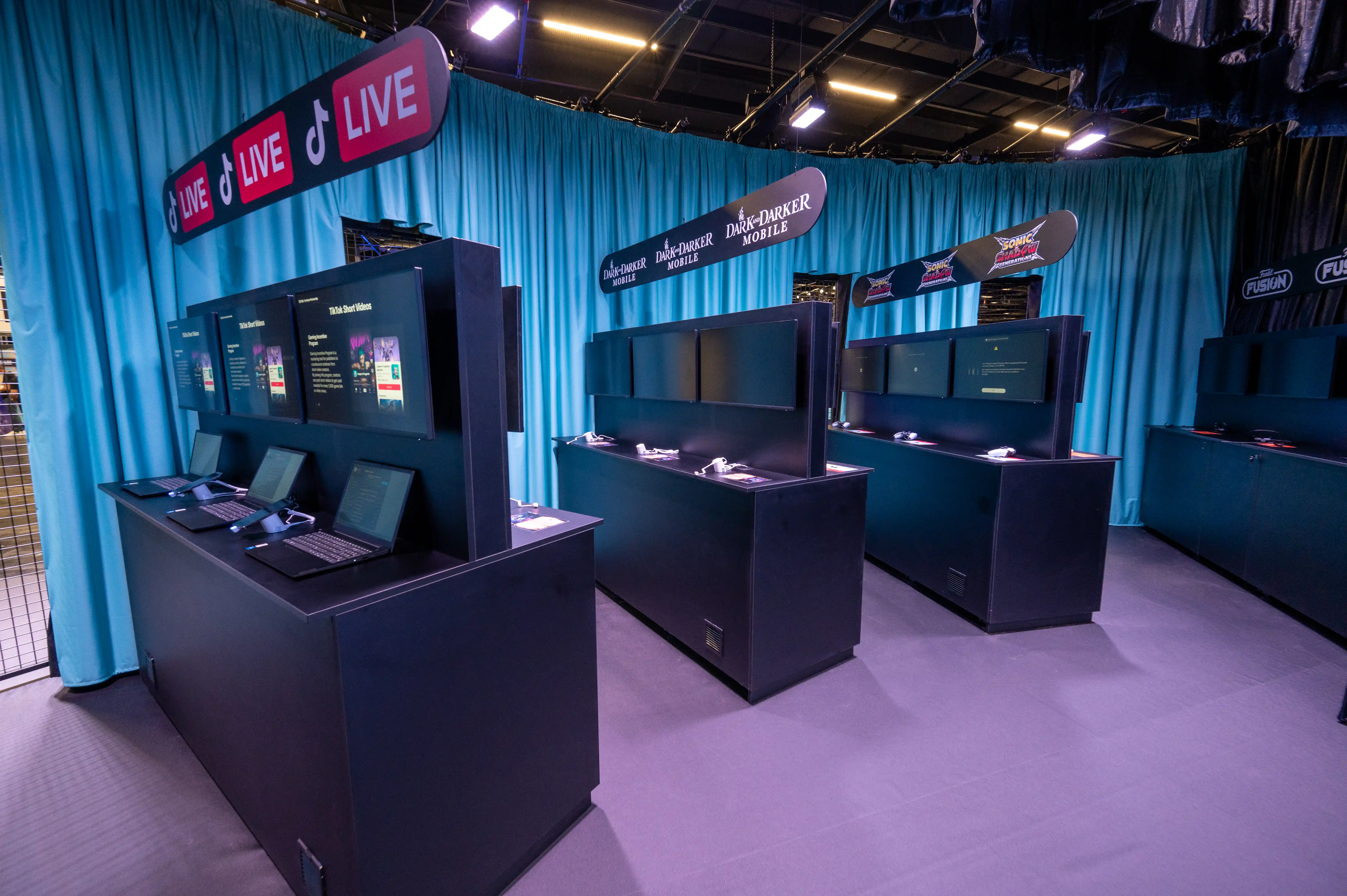 Gaming stations with laptops and screens under TikTok Live signs in front of light-blue curtains at Gamescom.