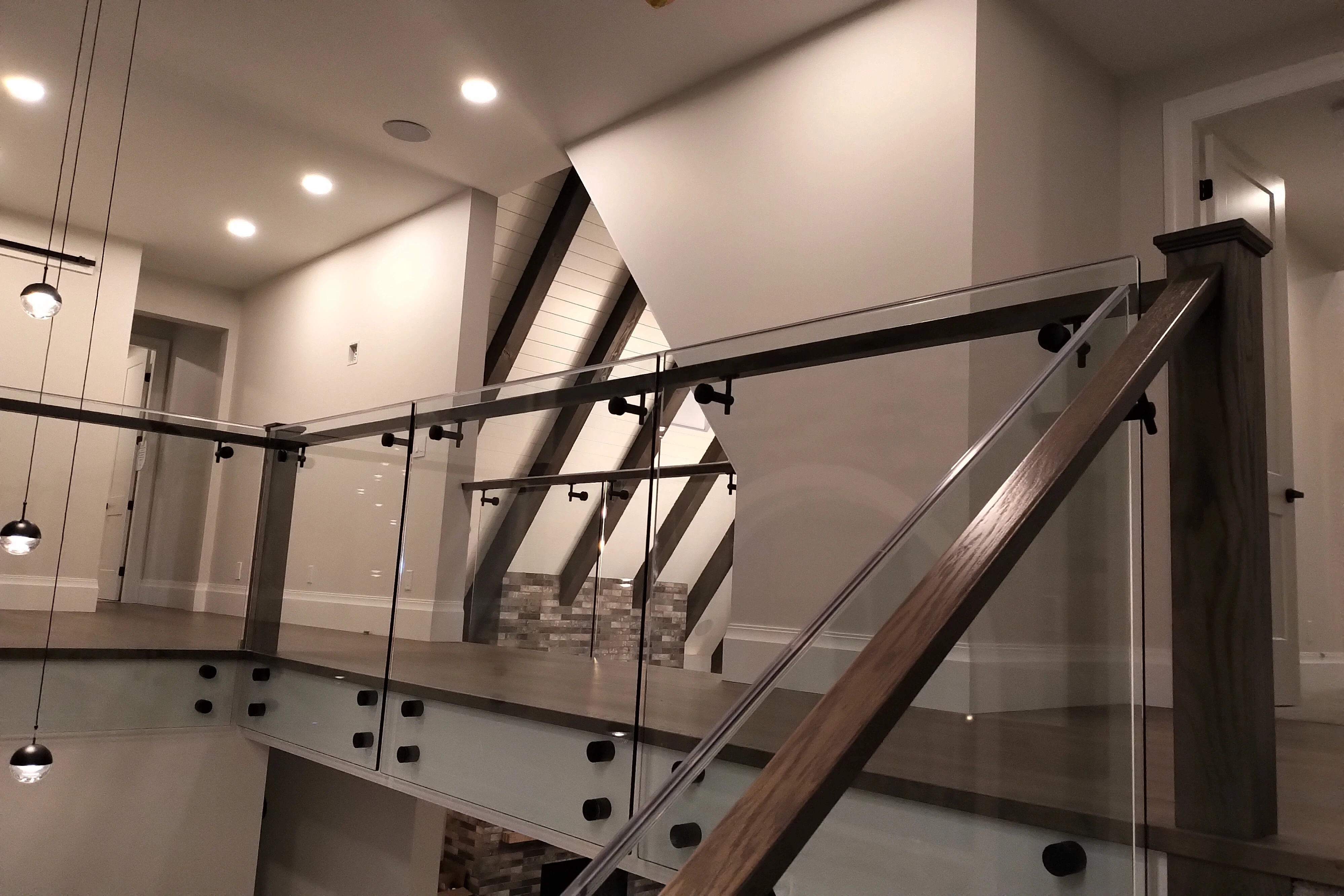Interior glass stair railing with black standoff fittings, a slim top rail, and a wood handrail in a modern BC home