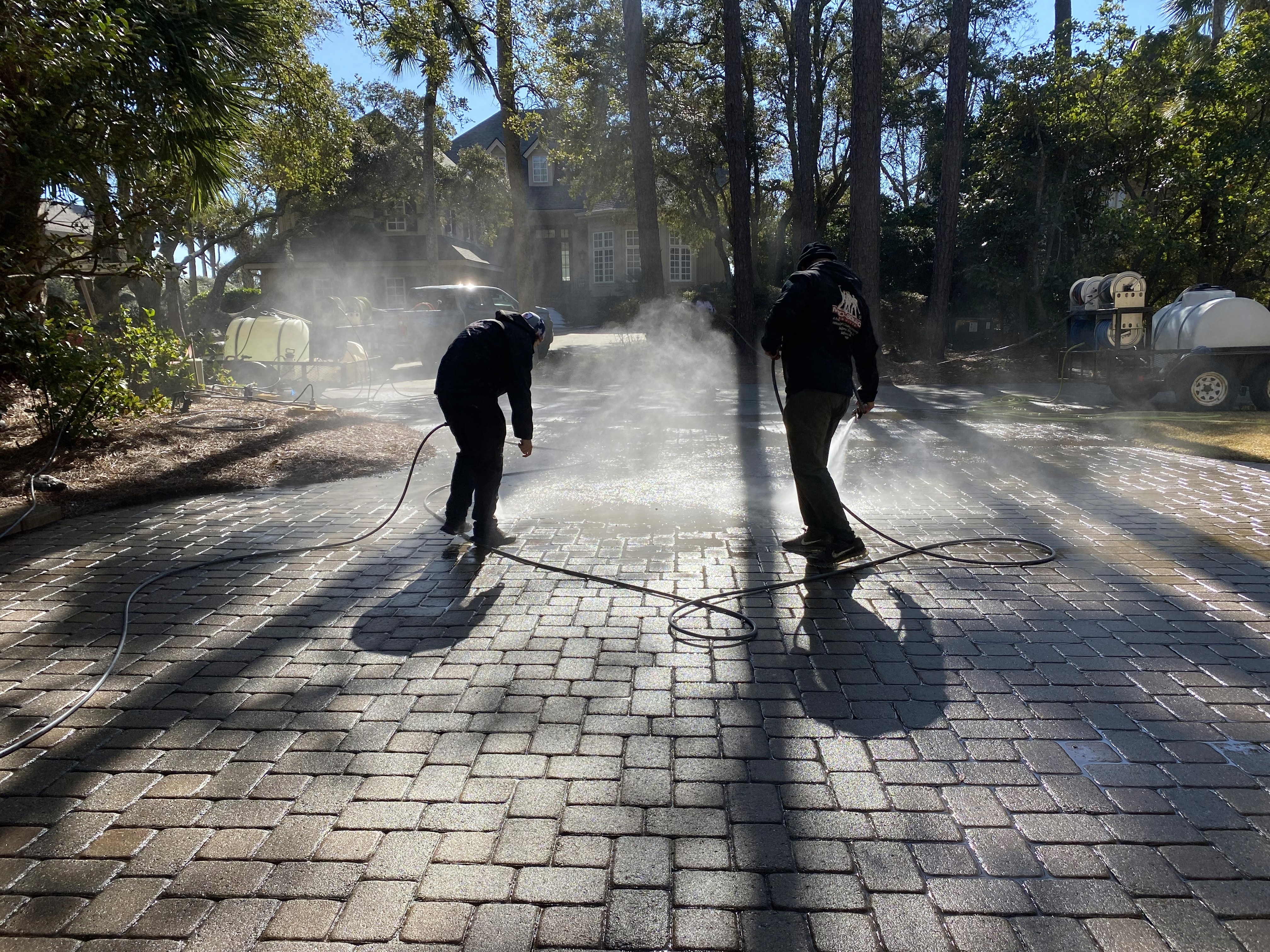 Technician using soft/power washing equipment—hose and spray applied to home exterior