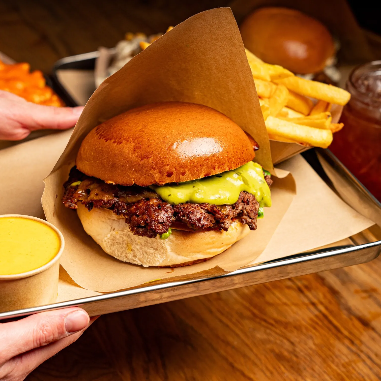 A hand holding a tray with a burger, fries, and a drink, arranged on paper.