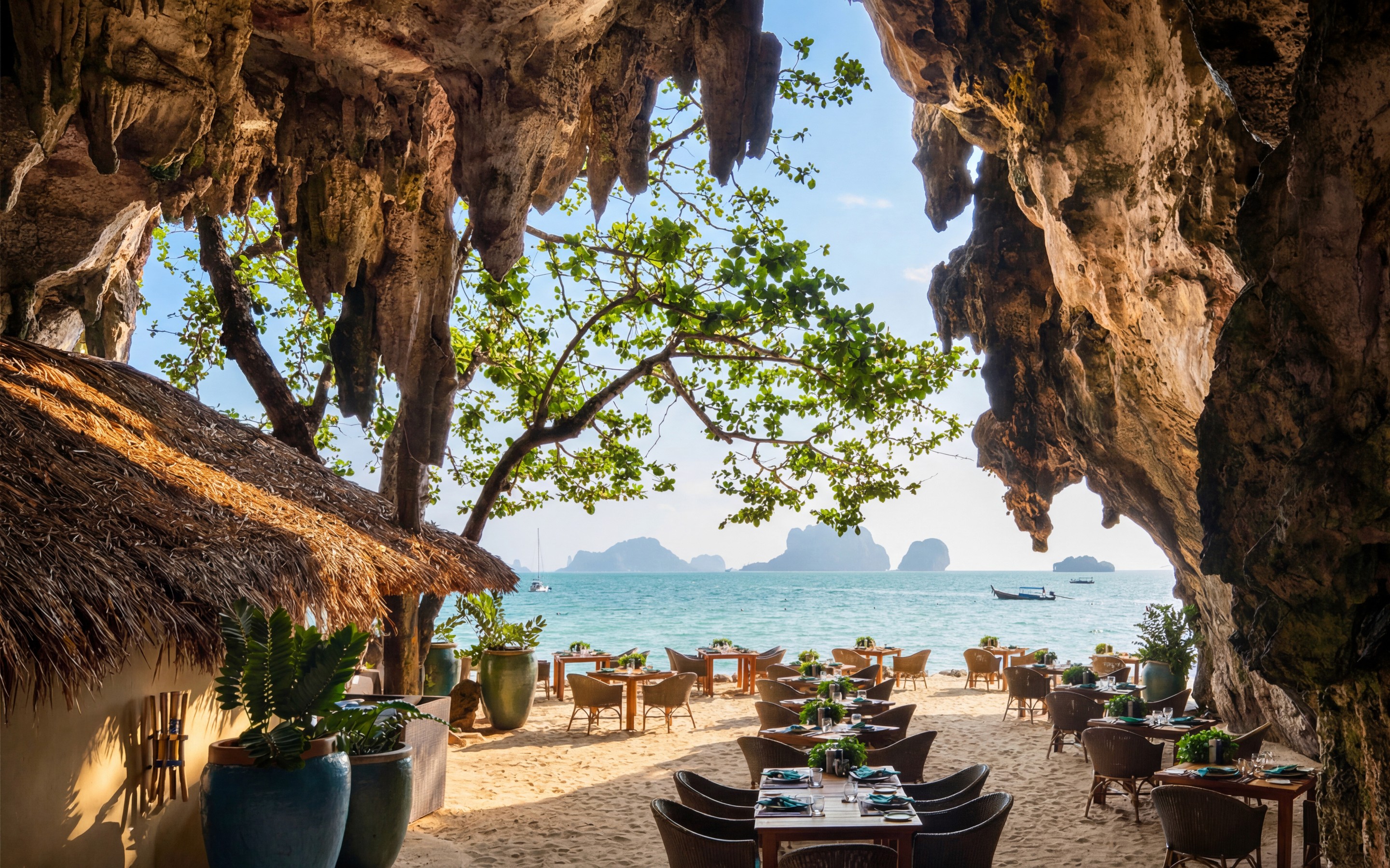 Beachside dining area set beneath limestone rock formations, with tables facing the sea in Krabi.