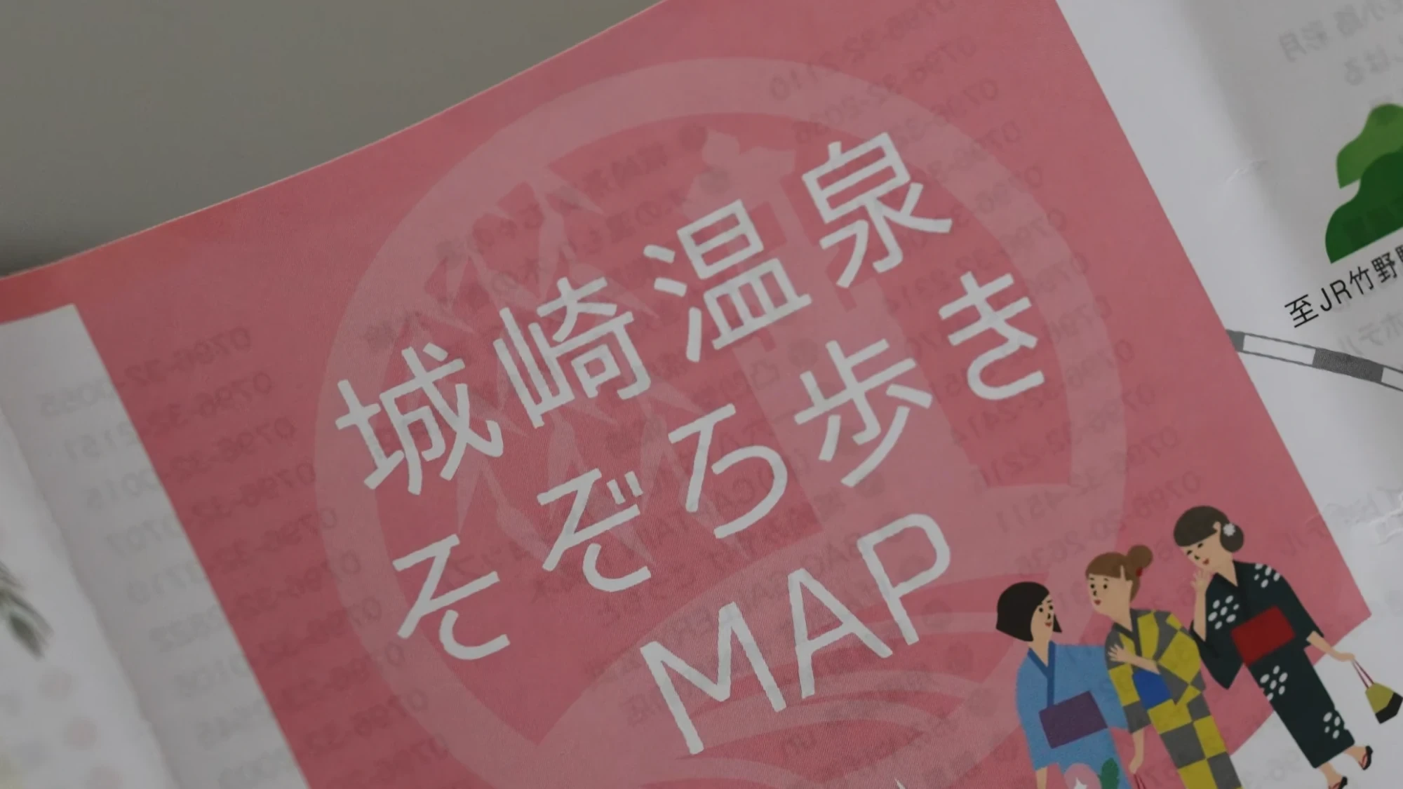 A hand holding the Kinosaki Onsen strolling map with the canal and bathhouse route printed across it.