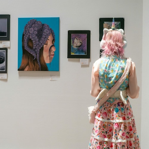 Pohled do Scholastic Gallery s uměleckými díly a jedním návštěvníkem prohlížejícím si exponáty