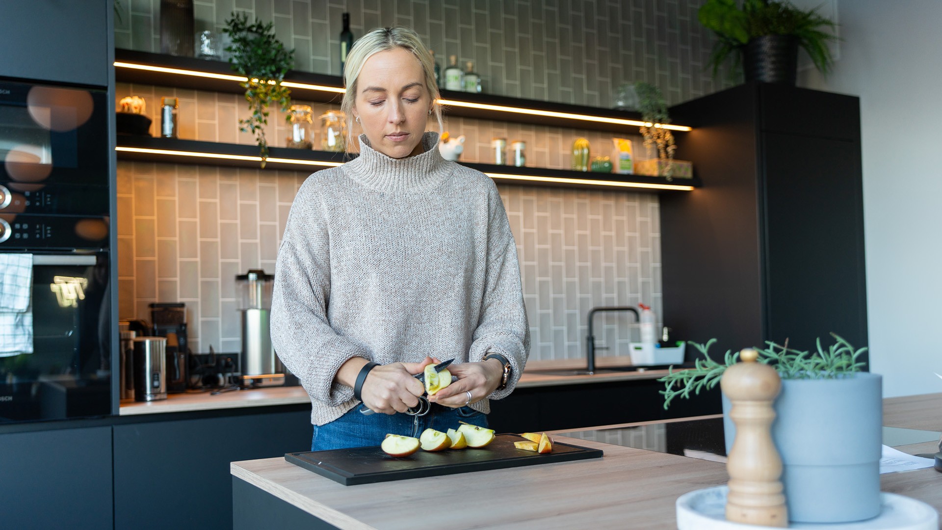 Eine Person steht in der Küche und bereitet sich einen veganen Snack zu. Im Hintergrund stehen die relevantesten veganen Supplemente und Nahrungsergänzungsmittel, die für eine ausgewogene vegane Ernährung notwendig sind.