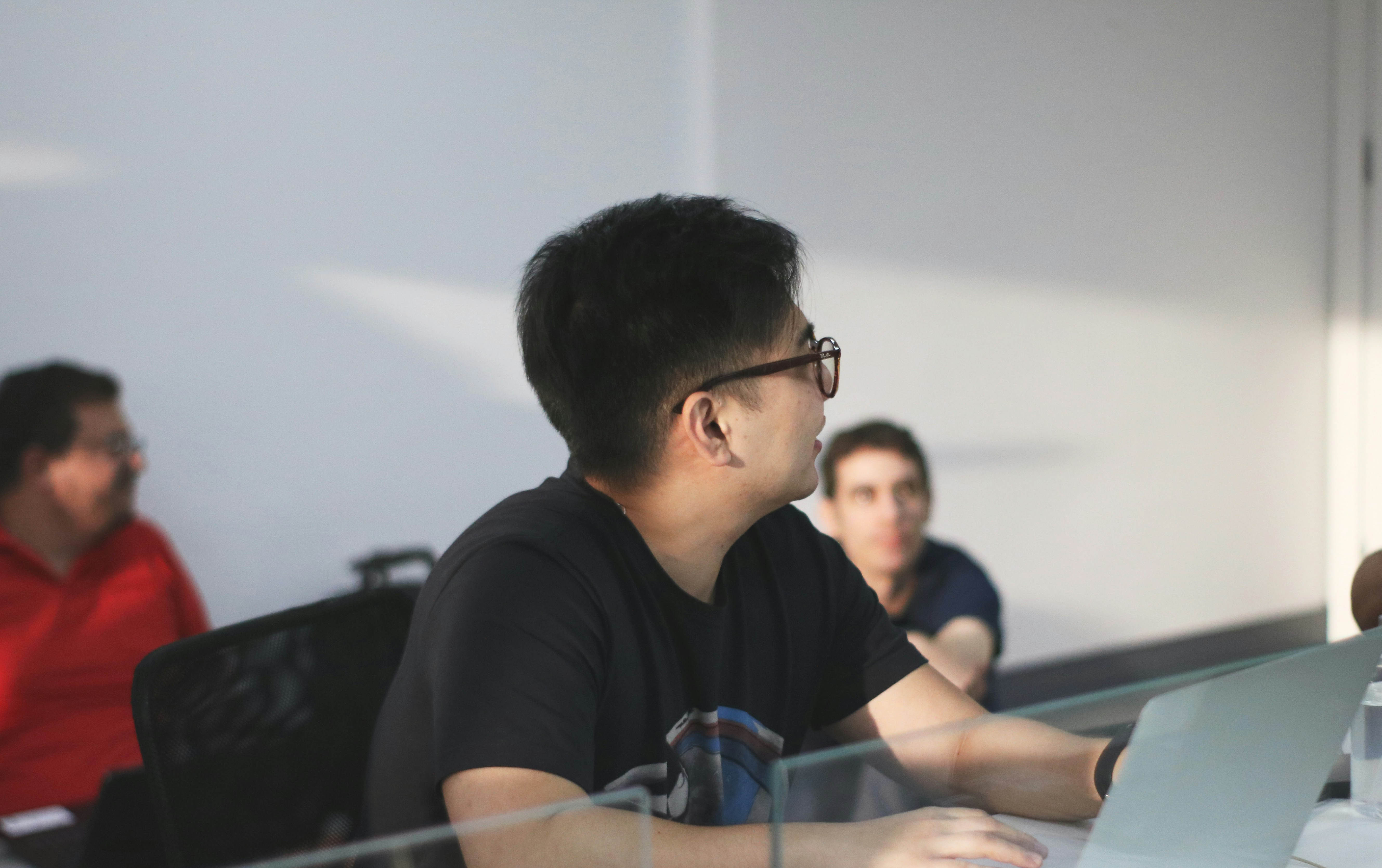 A woman with red hair and a black sleeveless top smiling confidently in a bright, modern indoor setting.
