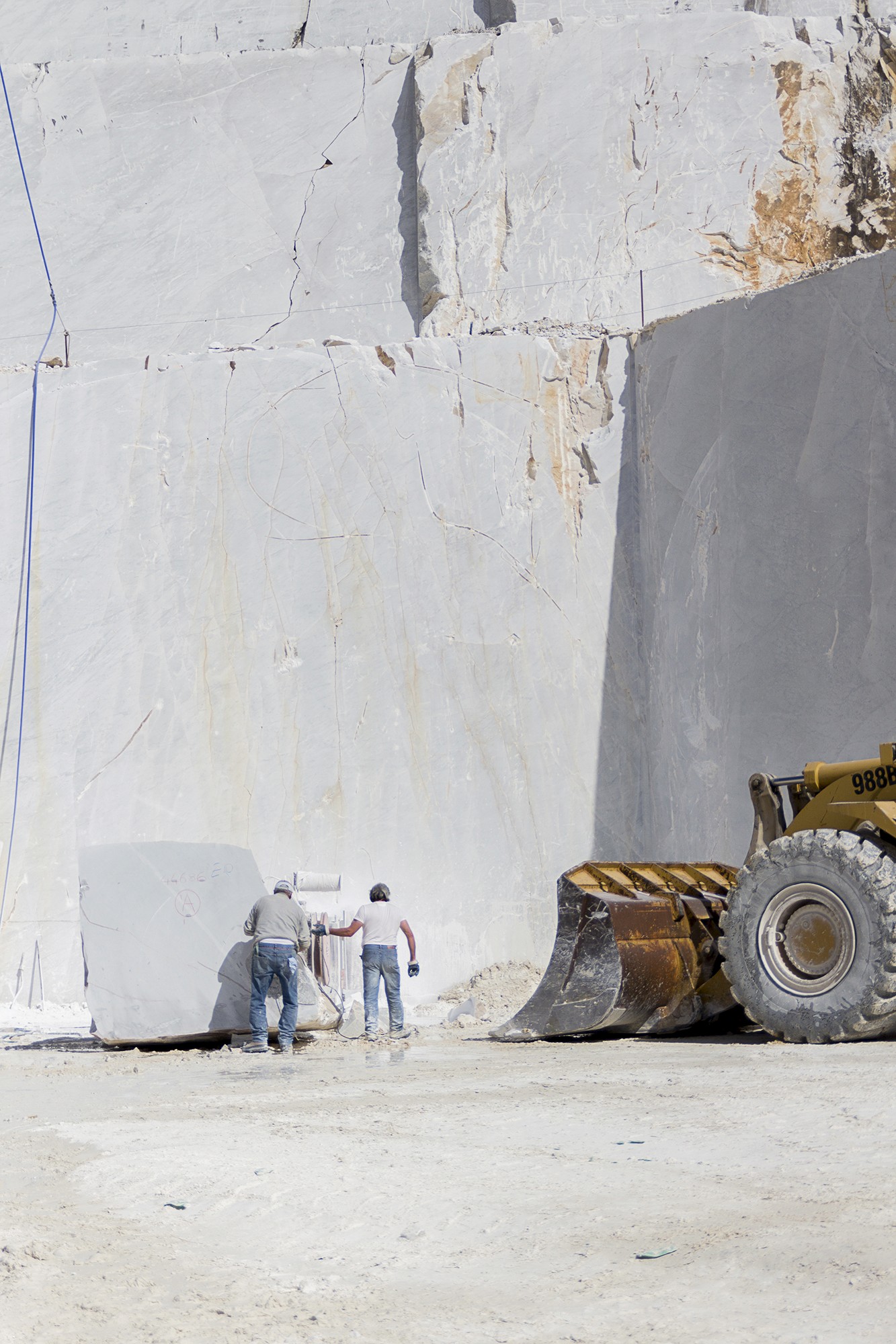 Photographie argentique de deux ouvriers face à une falaise de marbre travaillant autour d'un bloc de marbre dans les carrières de Carrare en Italie