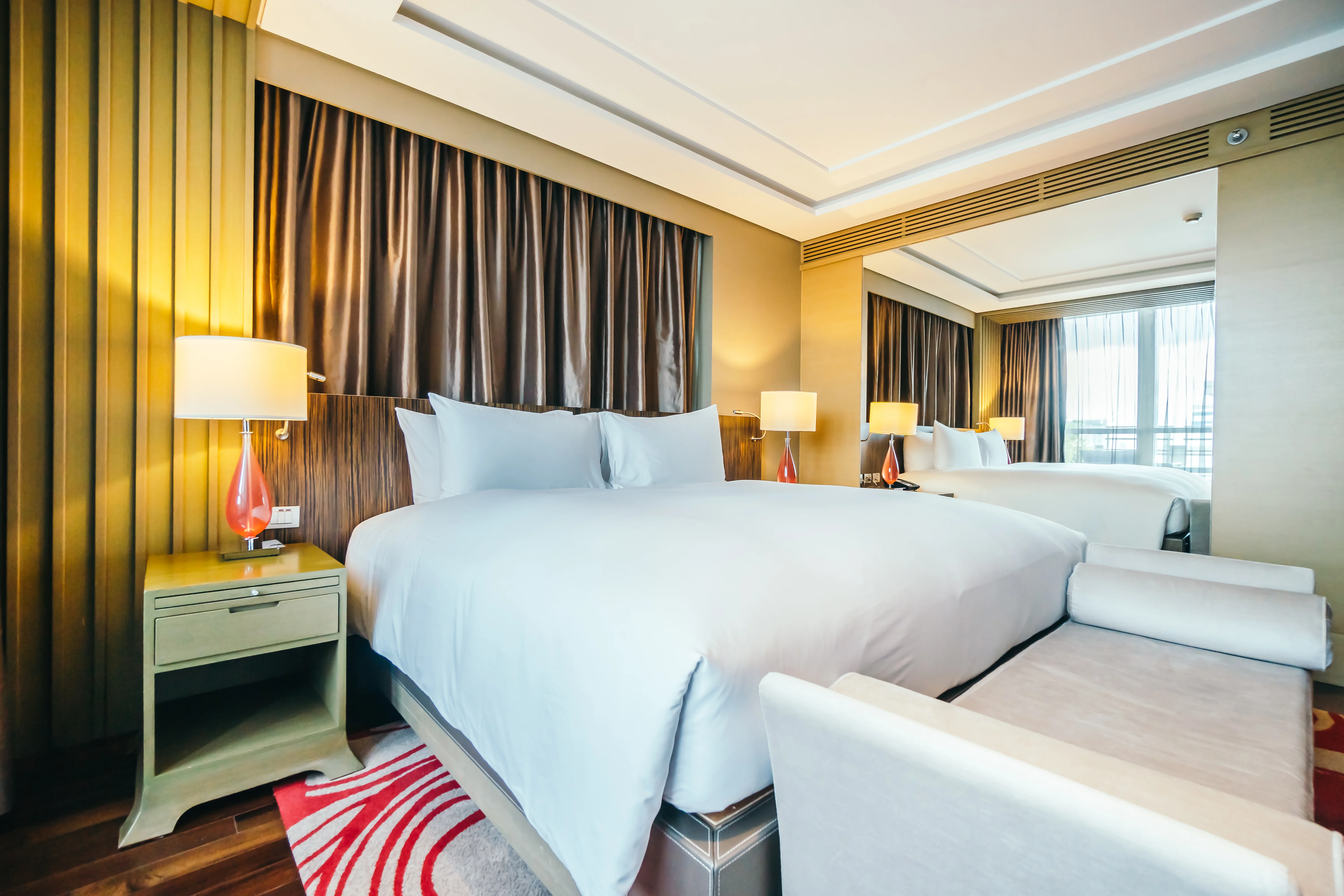 Modern gold-toned room with mirrored wall and twin beds