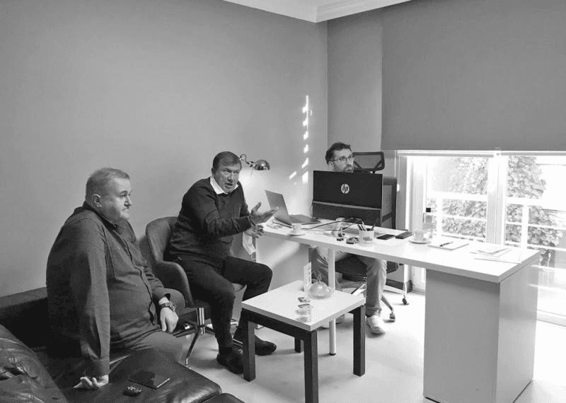 Monochrome fashion editorial of a model in an oversized white trench coat walking in profile on a high-key background.