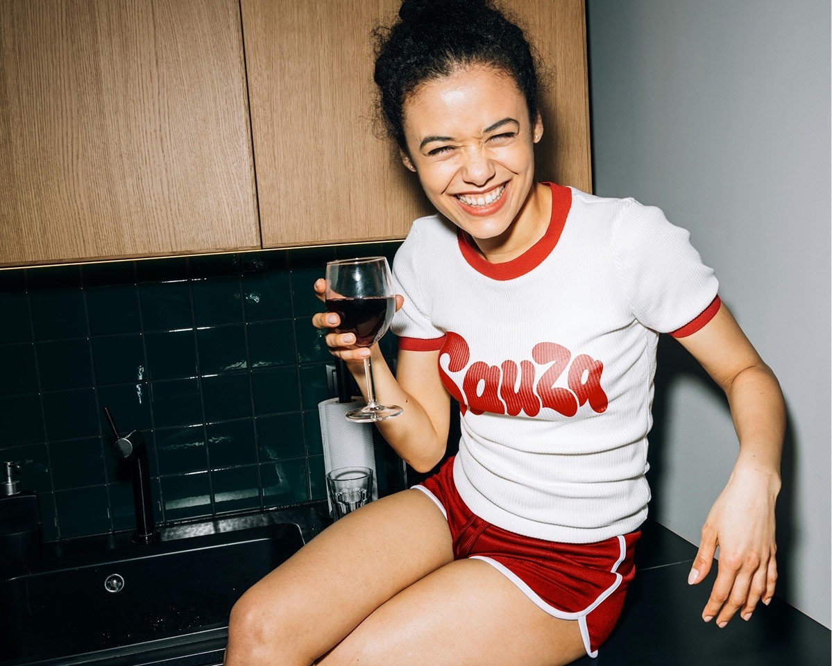 Sauza Pizzeria lifestyle photo of a woman in branded apparel beside an open pizza box.