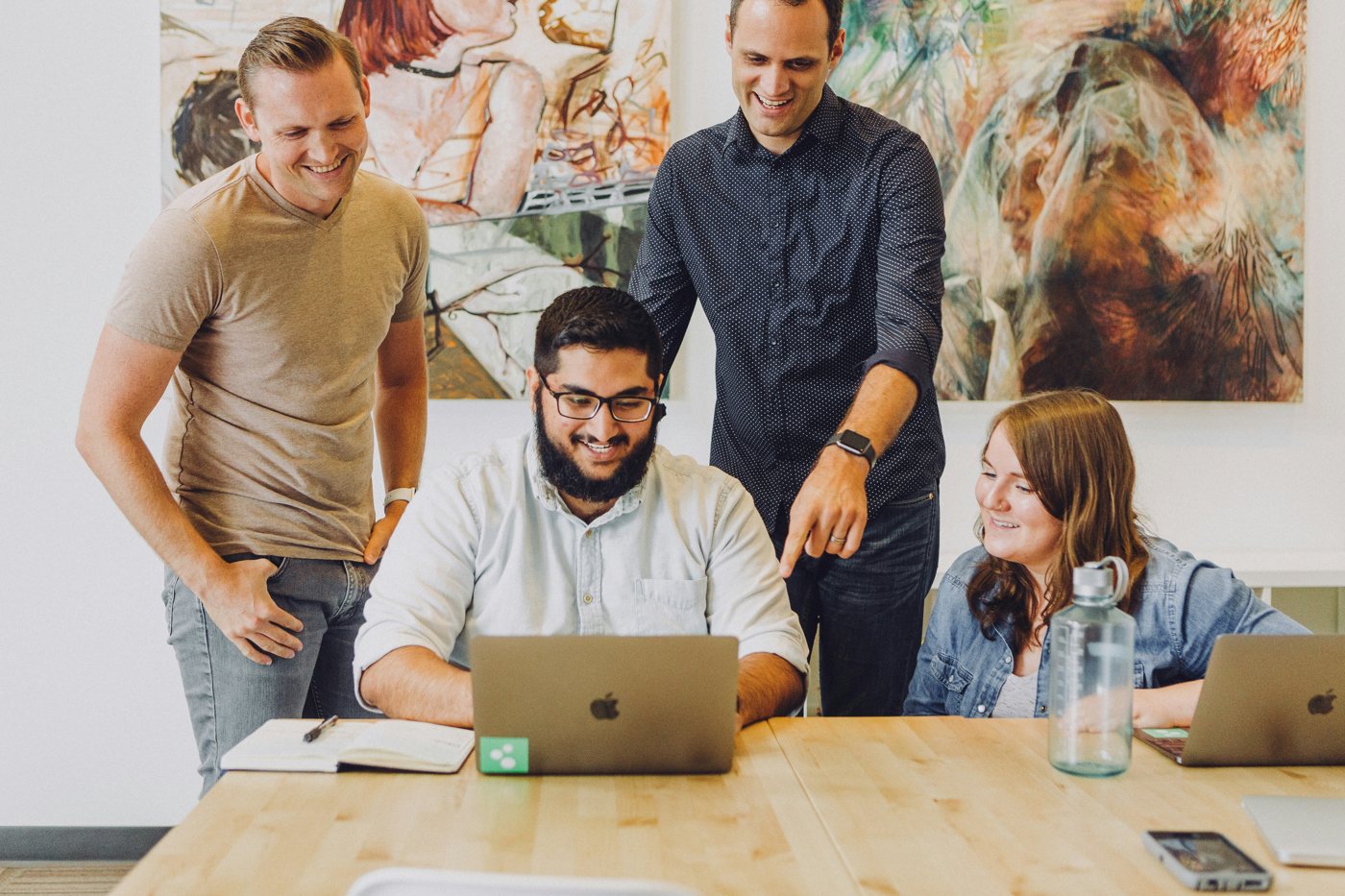 Four colleagues gathered round a laptop at a shared desk, talking through a plan