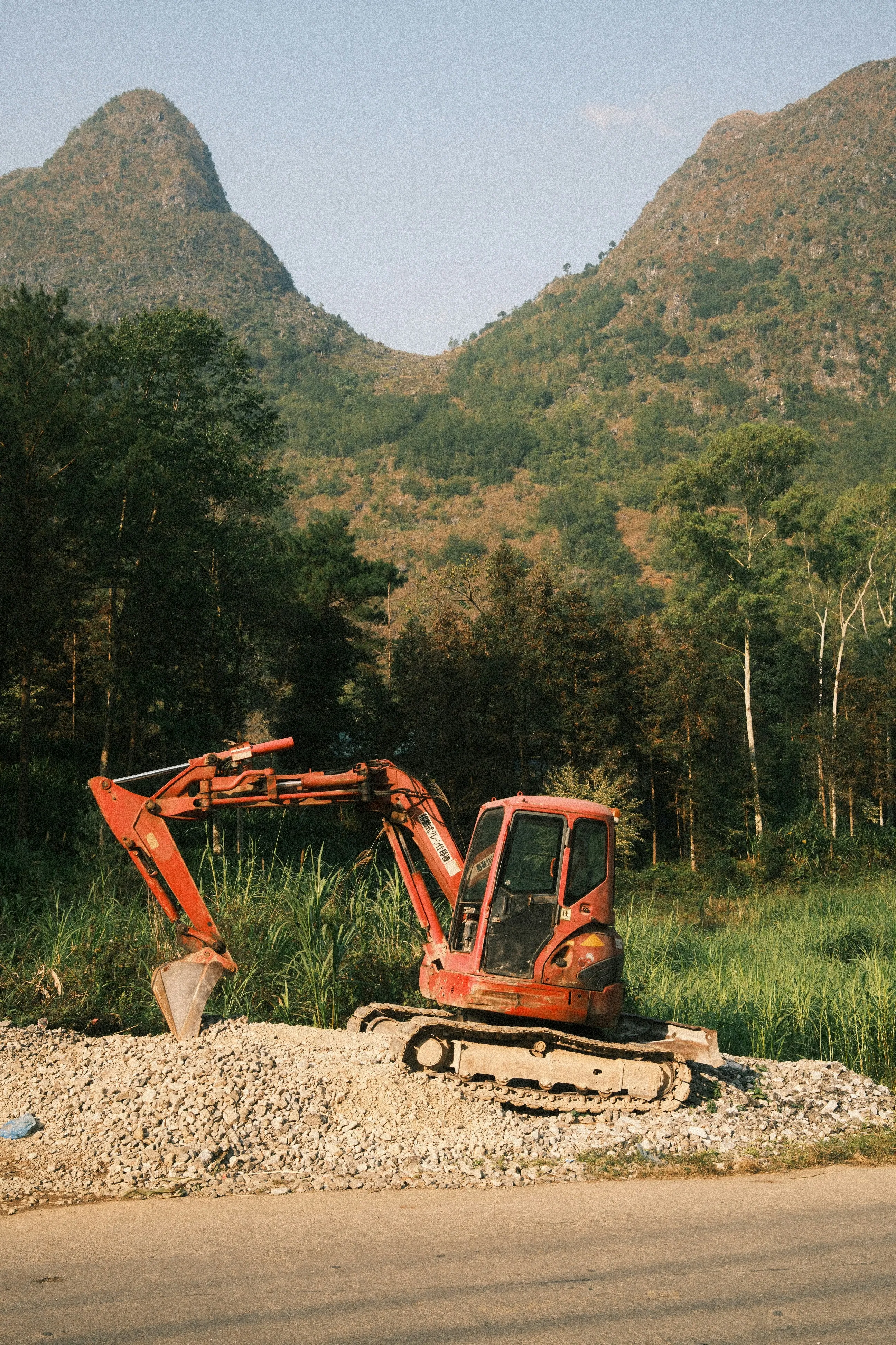 An orange excavator sits on gravel with mountains behind.