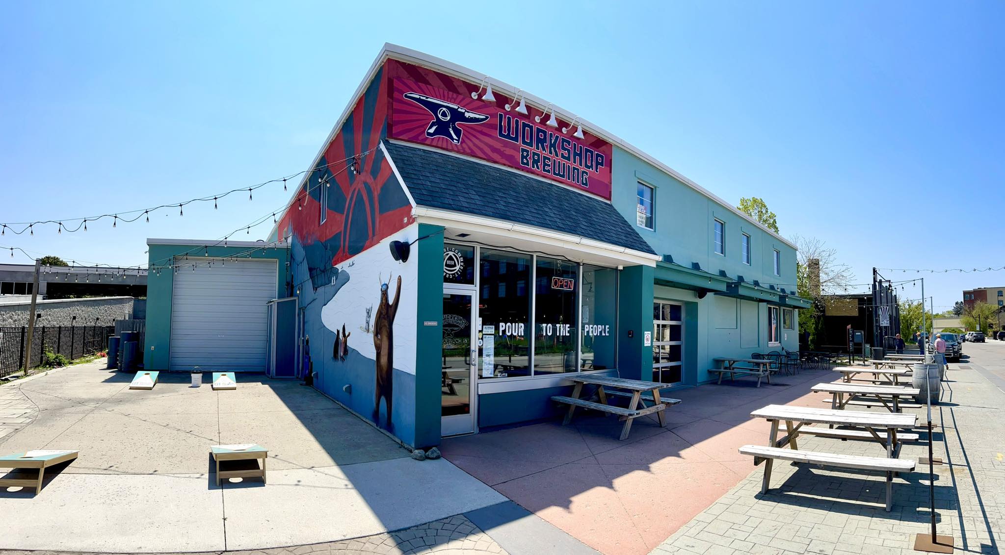 the interior of six spoke brewing company, with wooden picnic tables, kegs in the background ,and lots of natural light.
