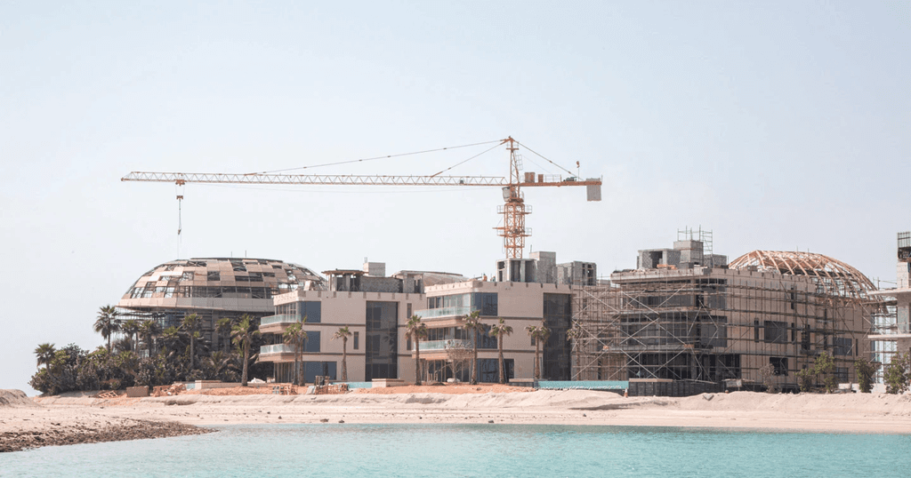 A large building under construction on the beach at The World Islands, showcasing cranes and scaffolding against the ocean backdrop.