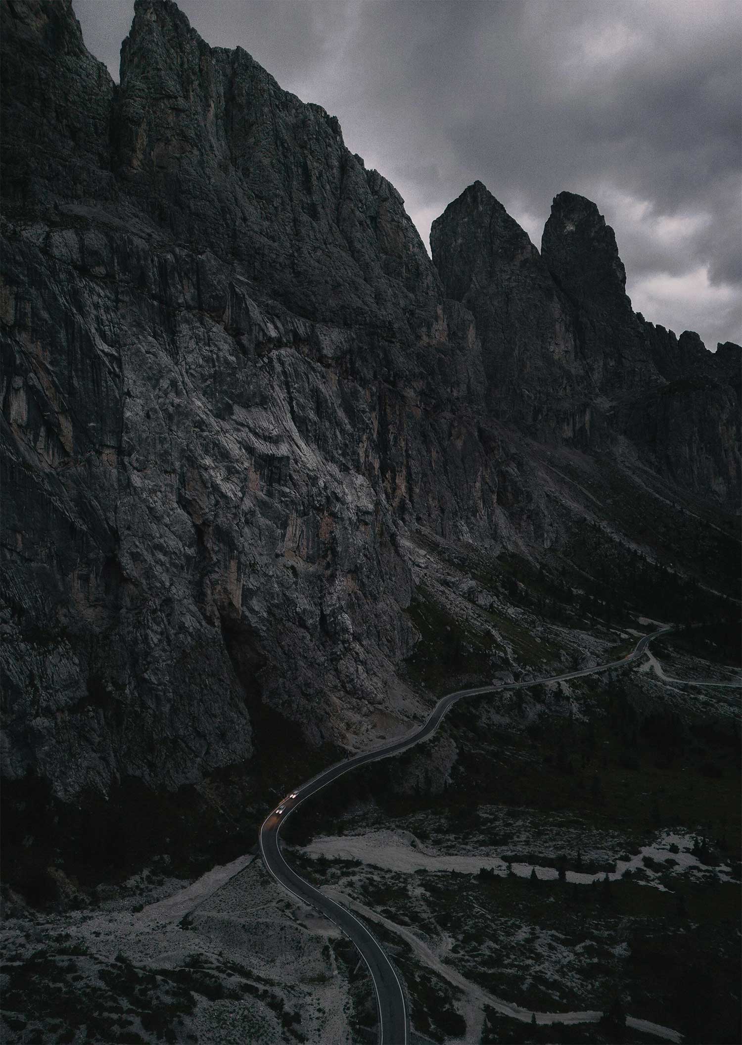 Winding mountain road with two cars under a cloudy sky.