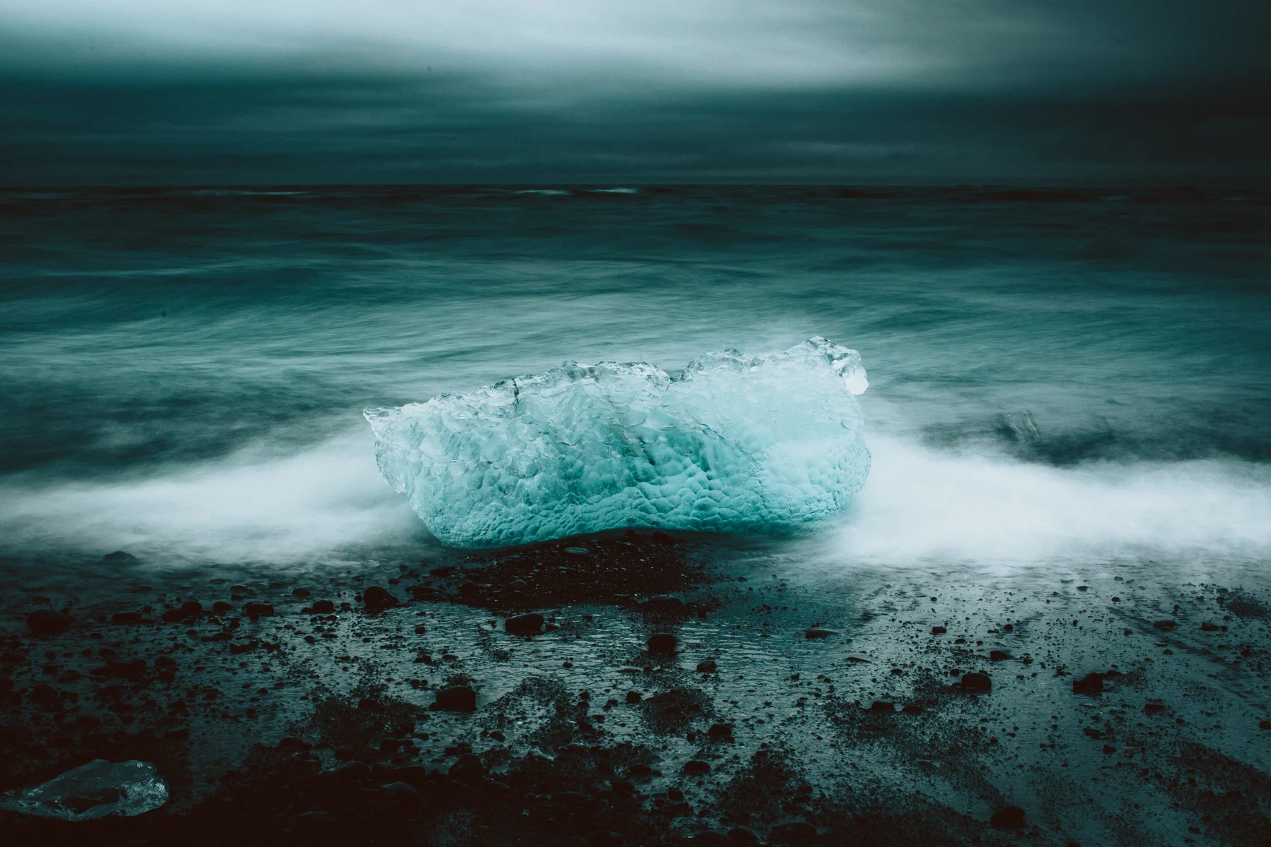 A block of glacier ice on black sand with surf blurring around it
