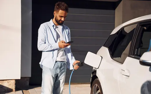 A photo of a man plugging a charging cable into his electric car