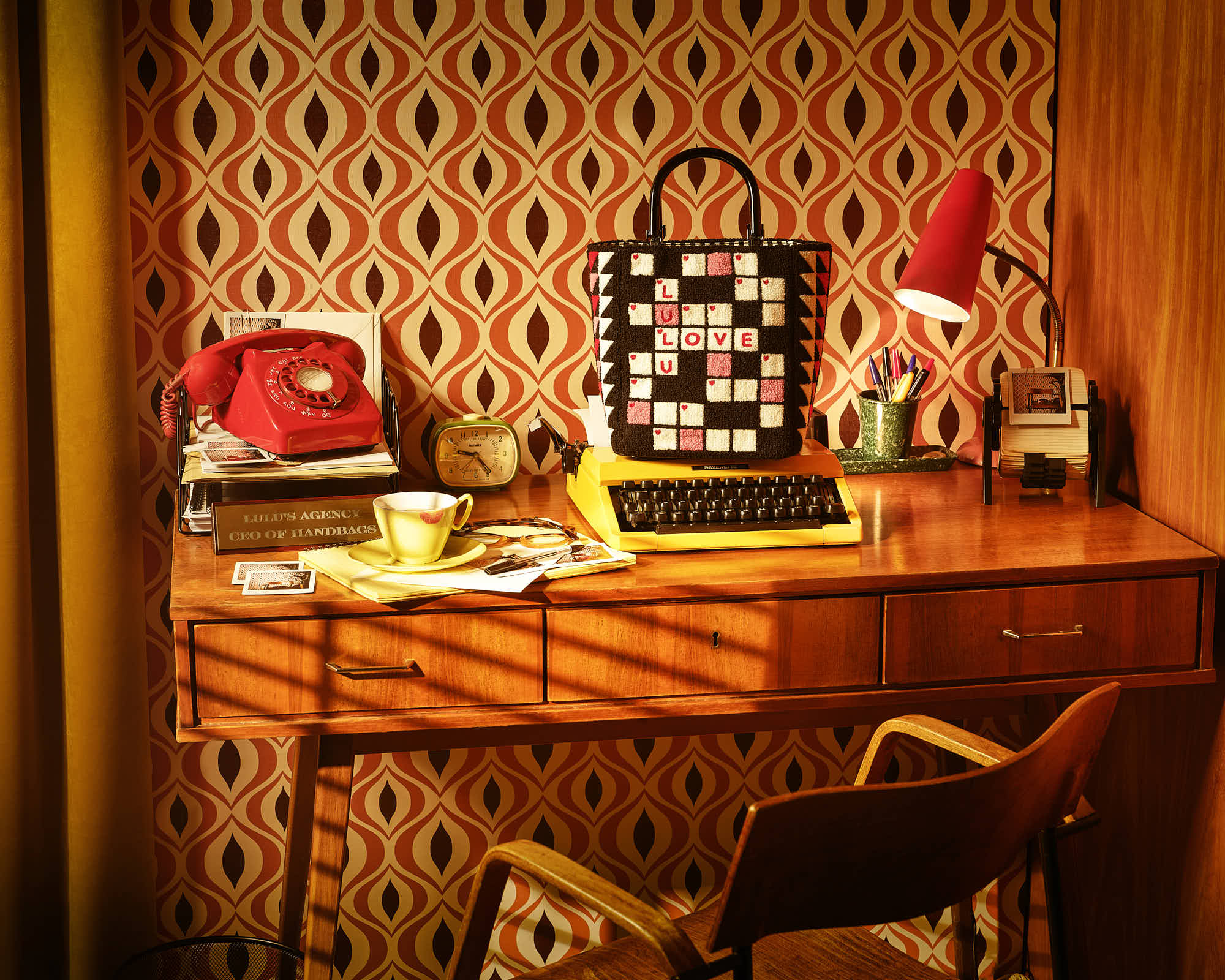 Retro office desk with a red rotary phone, vintage typewriter, and a stylish patterned bag.
