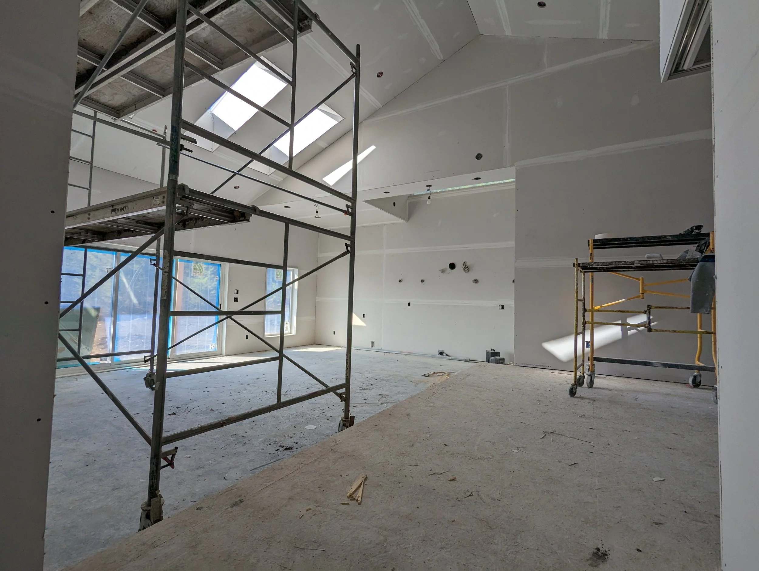 Modern two-story home with large glass windows, warmly lit interiors, and a balcony. Surrounded by trees and a manicured lawn at dusk. Cozy ambiance.