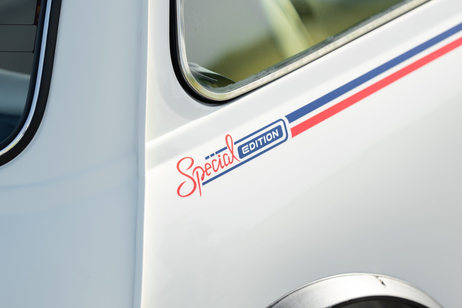 Close-up of a white vehicle with a blue and red stripe design, part of the door frame visible.