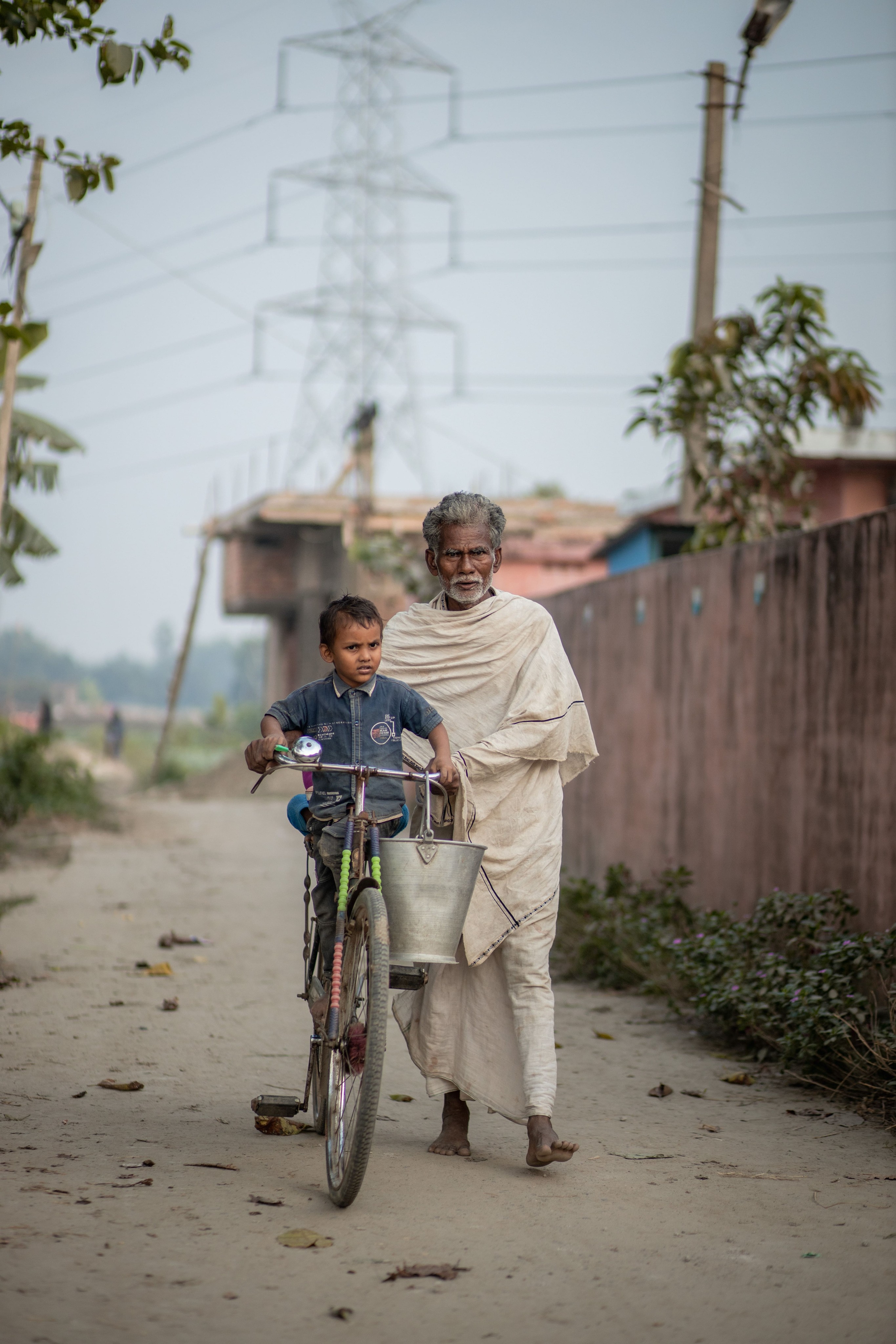 An old man walking with a bicycle and a small kid sitting on the bicycle in the village where Sunmeister’s solar cold rooms are installed