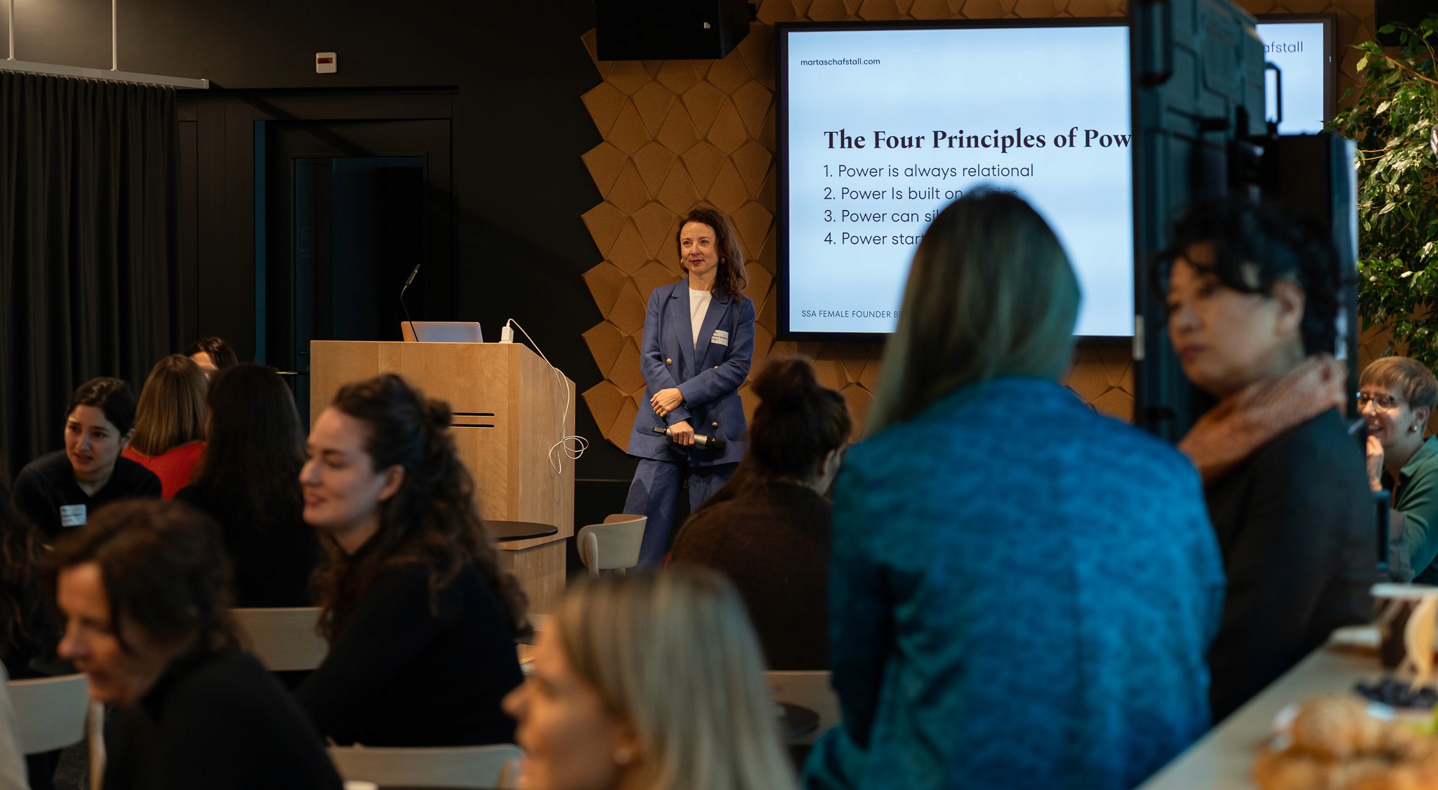 Man in a sweater smiling with arms crossed while standing by a wooden wall.