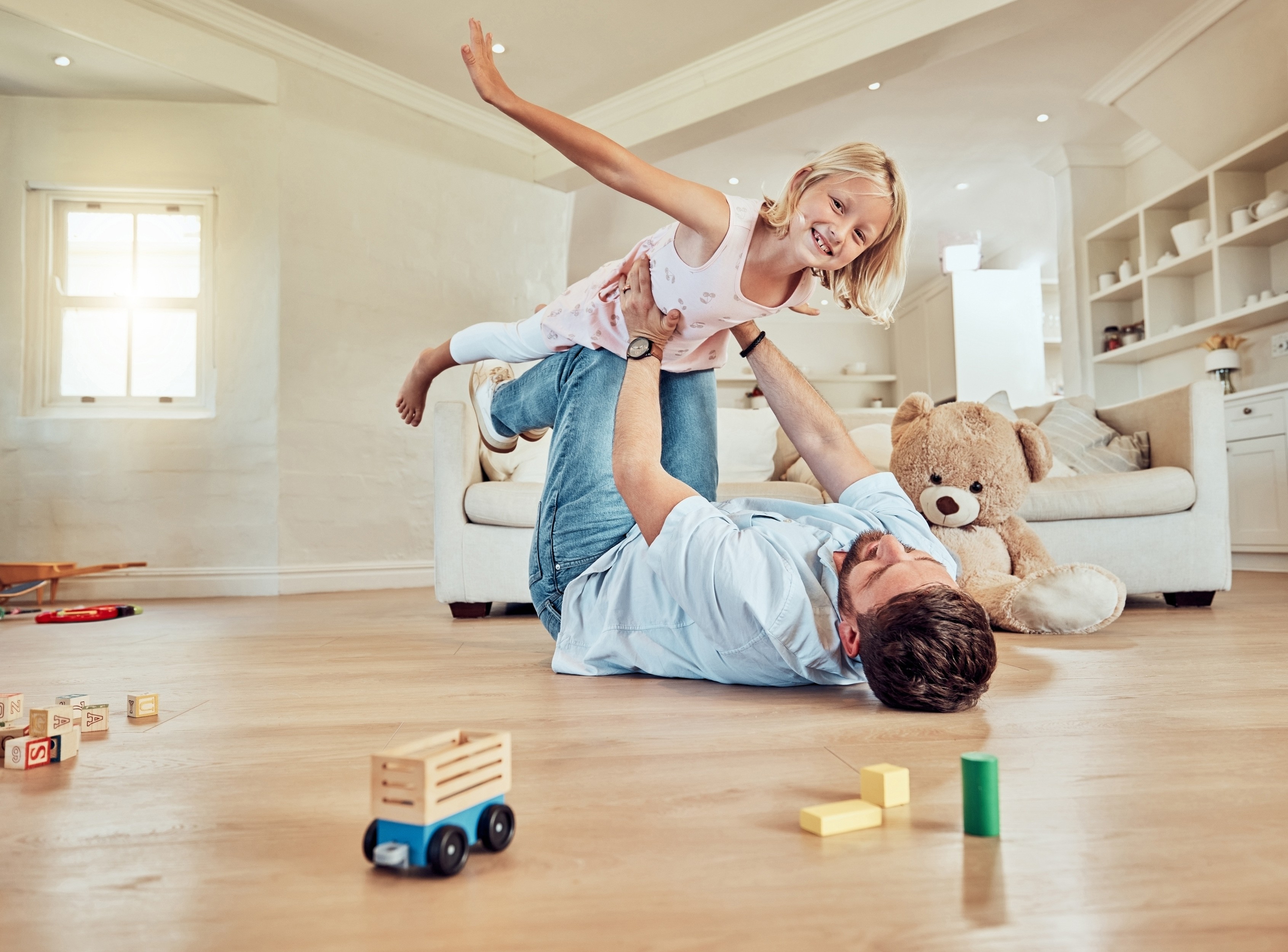 Dad playing airplane with his daughter on the living room floor in a Brisbane home, choosing safe flooring that handles rough play and everyday family life