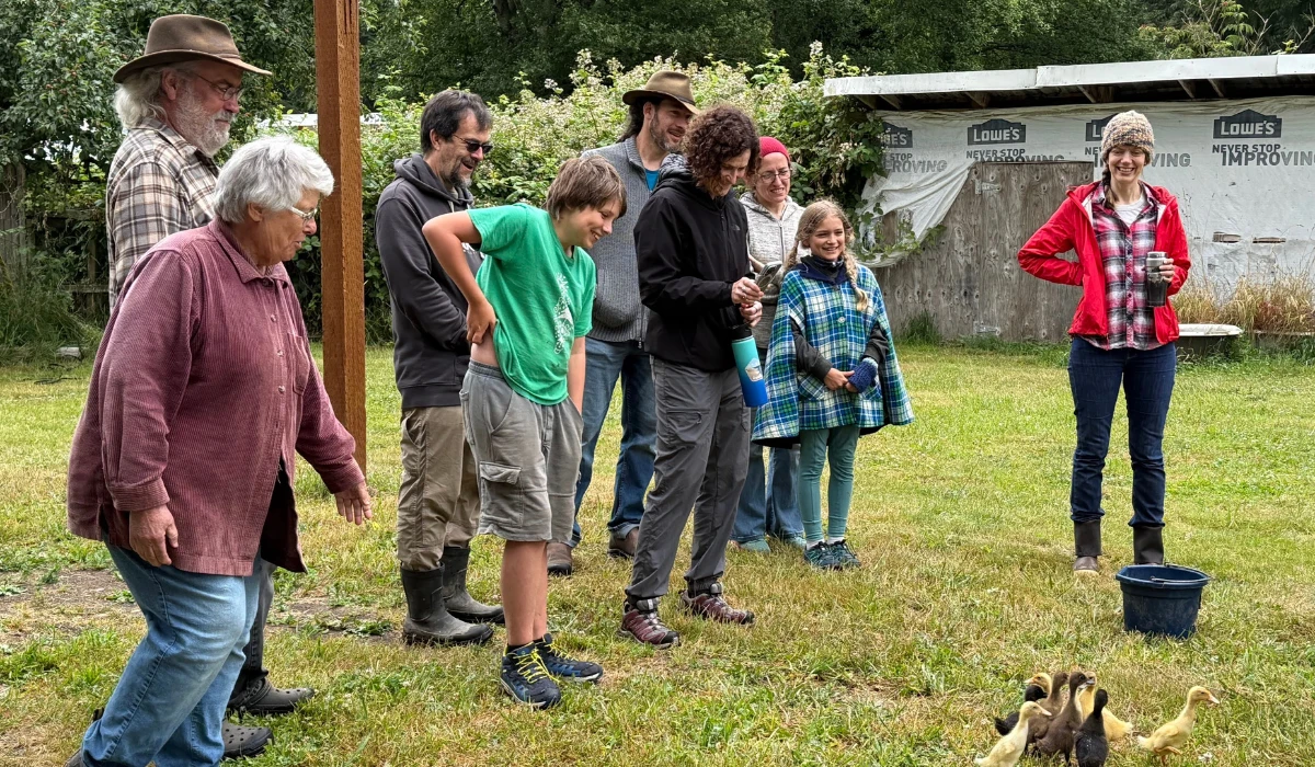 Neighbors and families share a communal meal at a long table inside a farm building at Rooted Northwest.