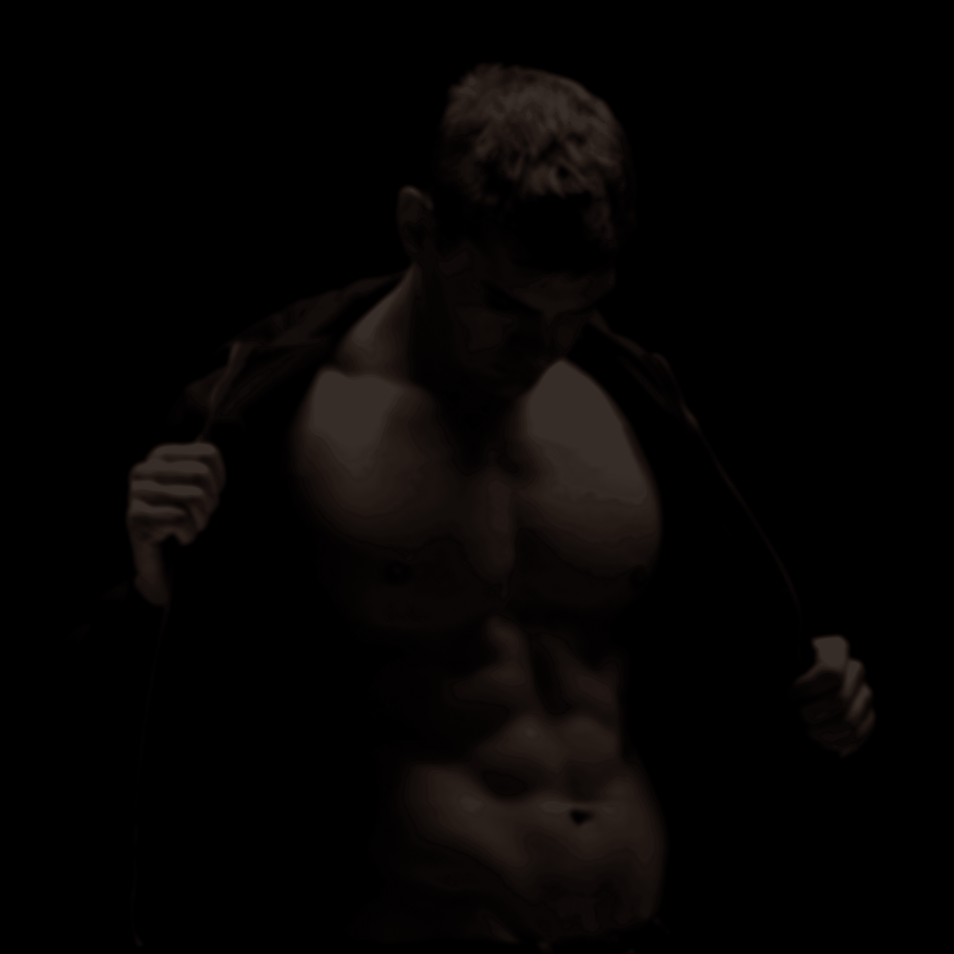 A man posing against a dark backround revealing a naked torso as he unzips his hoodie.
