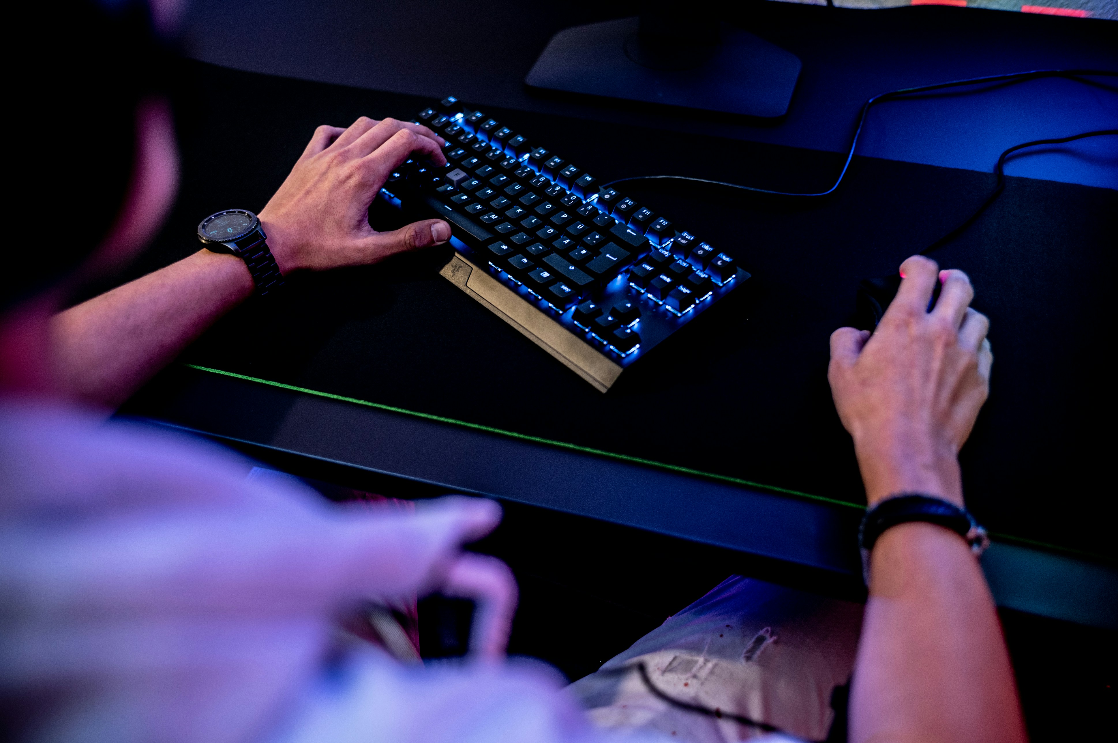 Person using a computer keyboard and mouse on a dark desk with blue lighting.