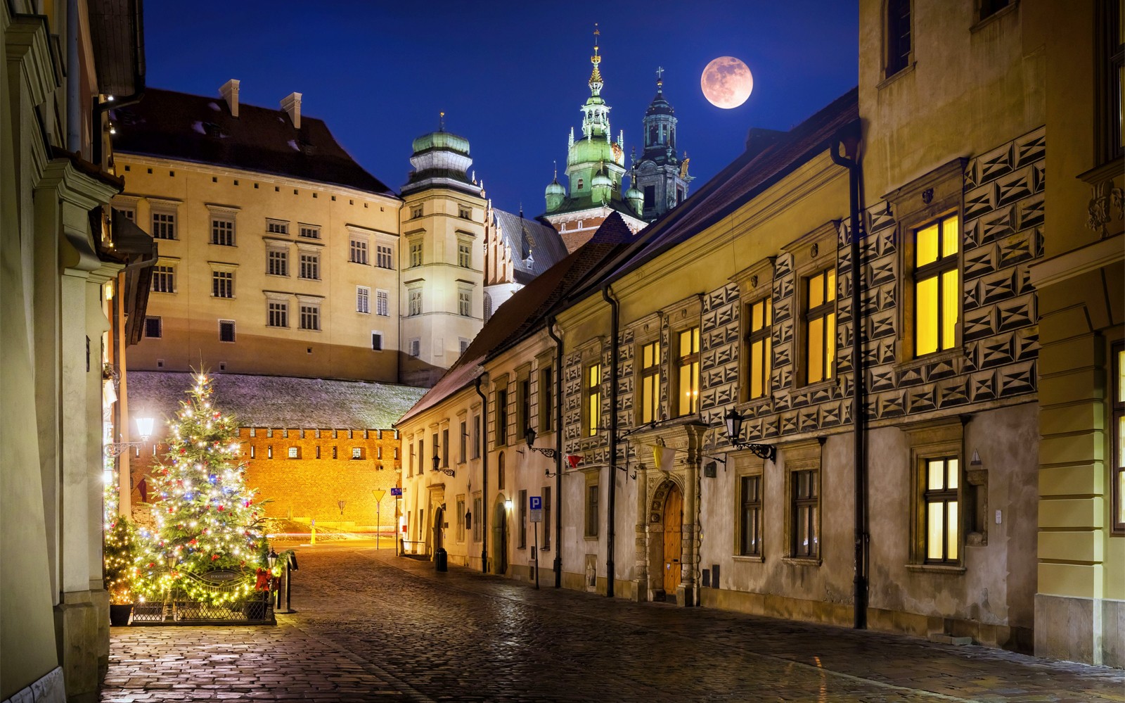 Krakow straat 's nachts met verlichte gebouwen en een volle maan.