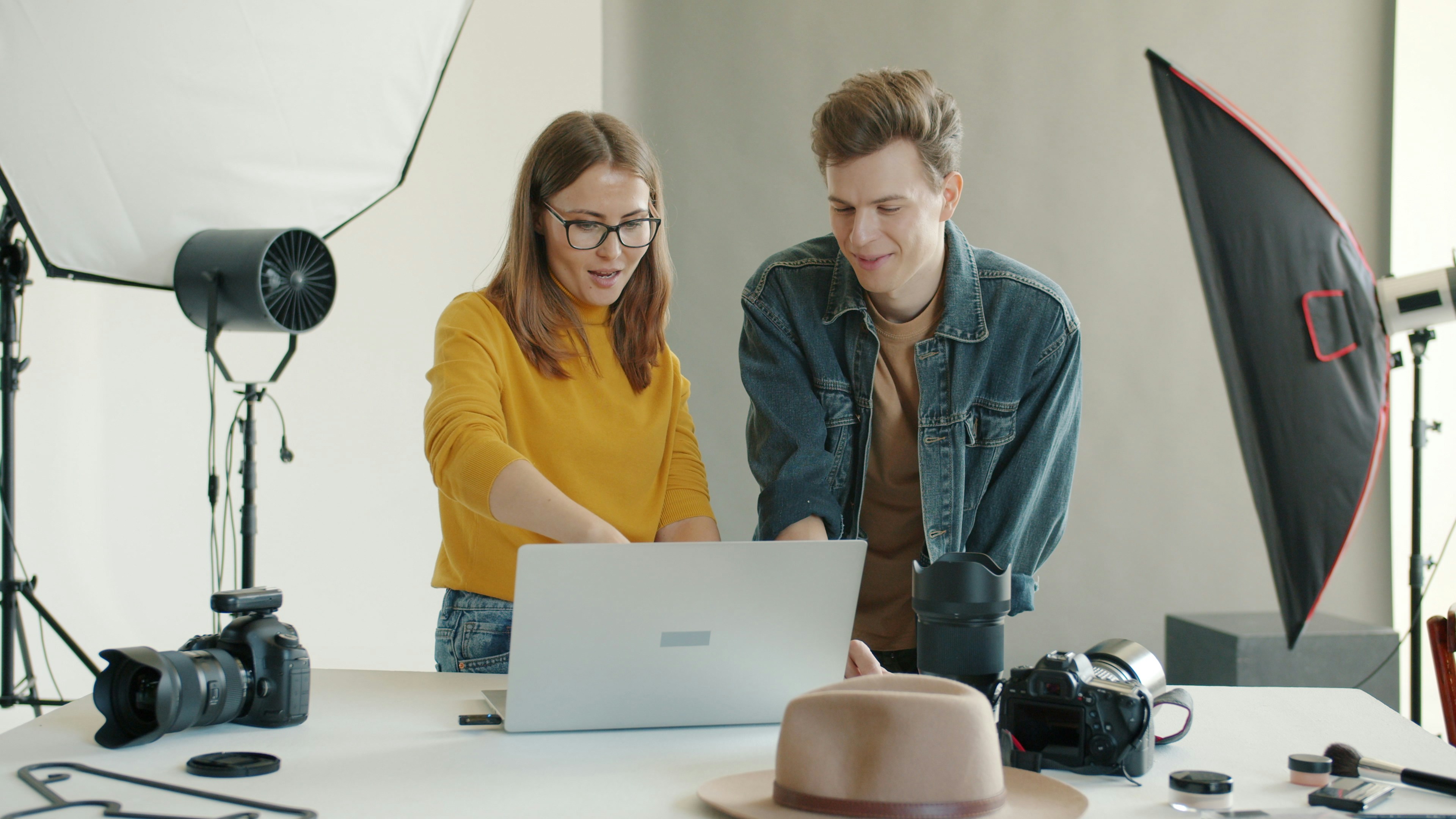 Two people working on a laptop with photography equipment.