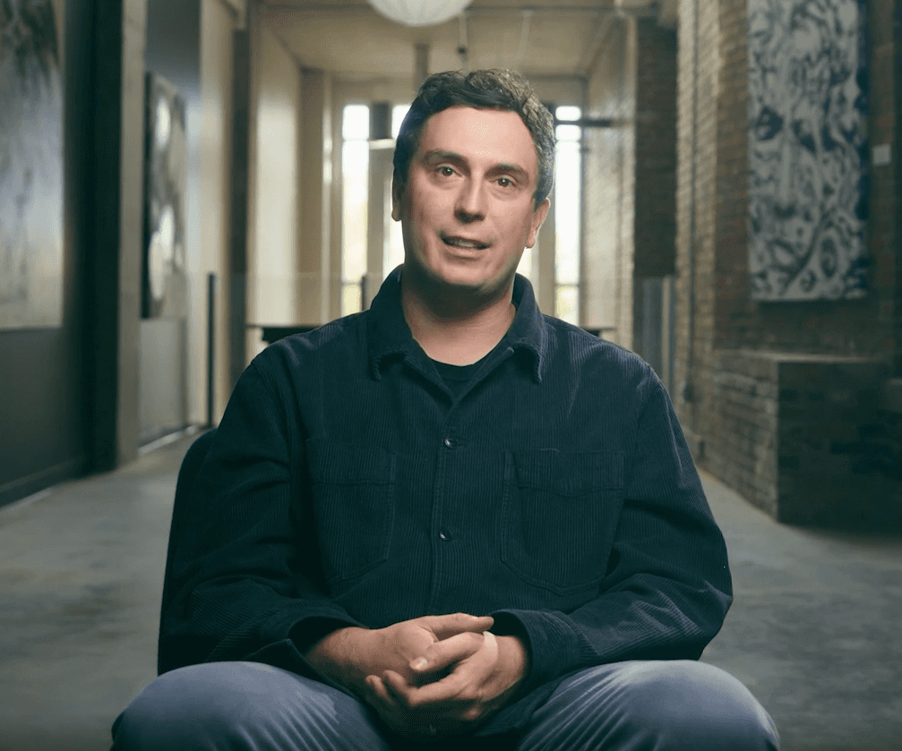 a man sits down for a interview in a room with natural light and exposed brick 