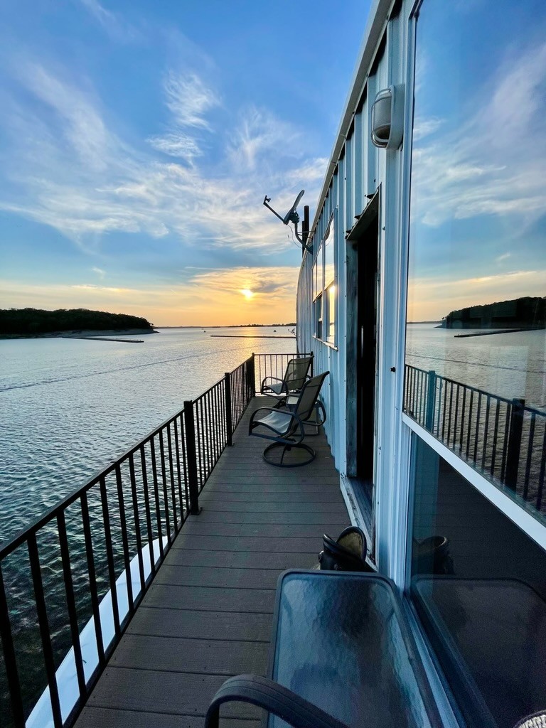 Sunset view from a waterfront balcony with chairs overlooking calm water and the horizon.
