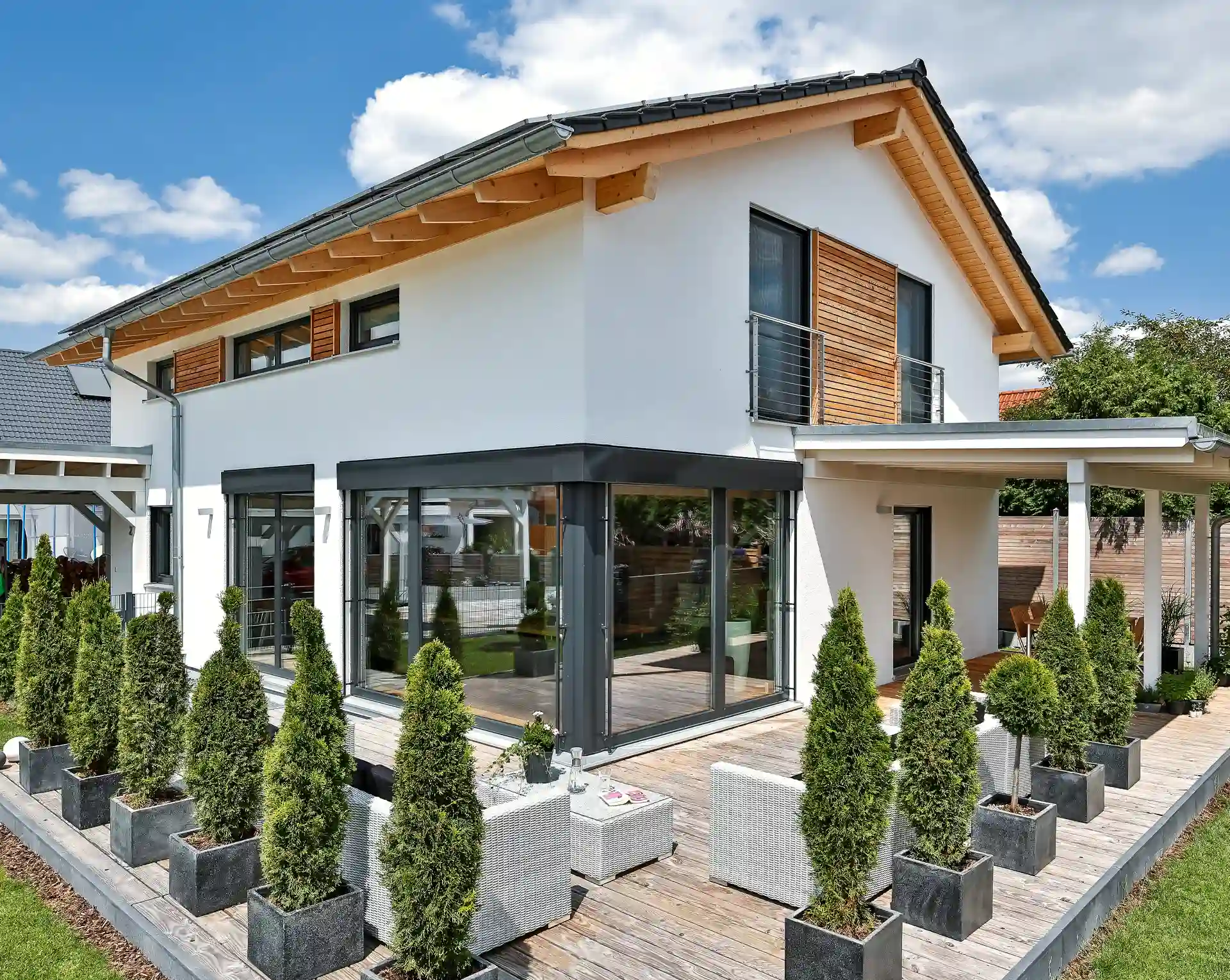 Modernes Einfamilienhaus mit Holzdetails und umliegender Terrasse mit Zierbäumen in gepflegten Kübeln.
