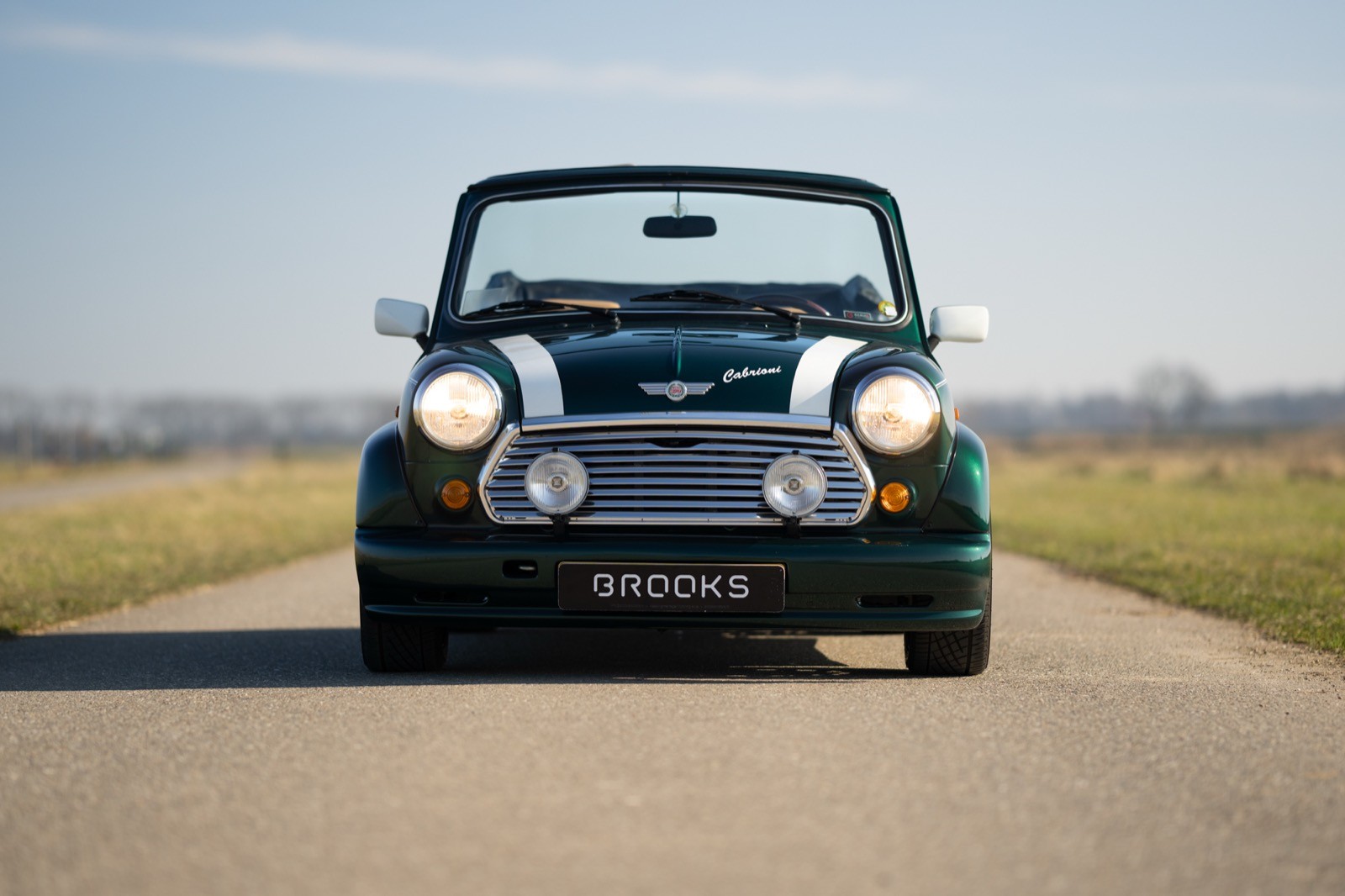 A classic black convertible car on an open road, with an expansive blue sky in the background.