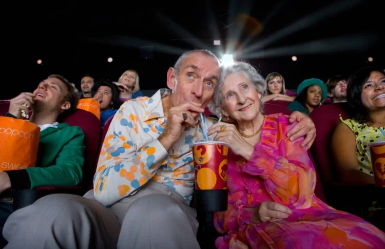 An aged couple at a movie theatre sipping cola.