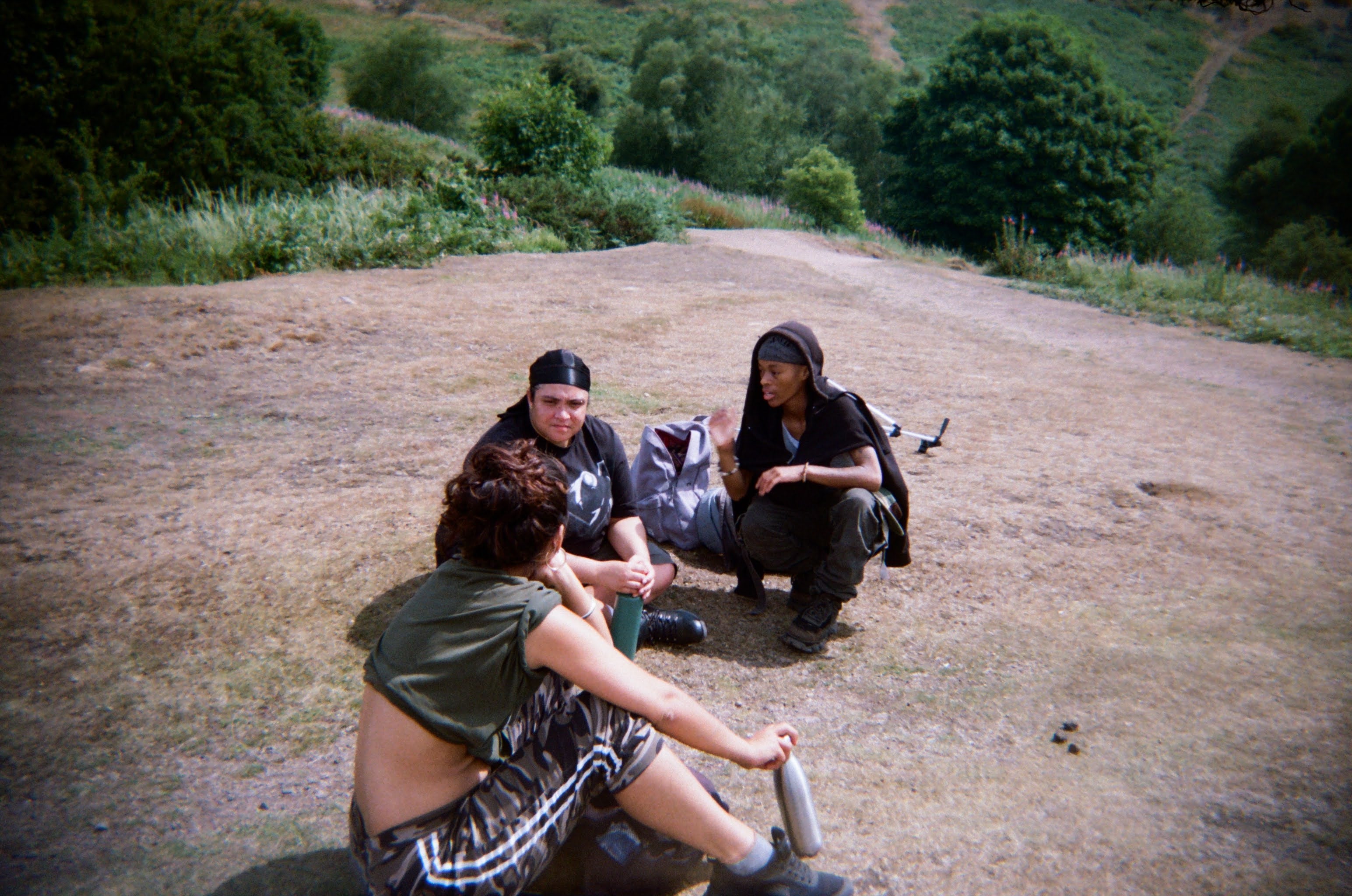Three people sit on the grass mid-hike, talking