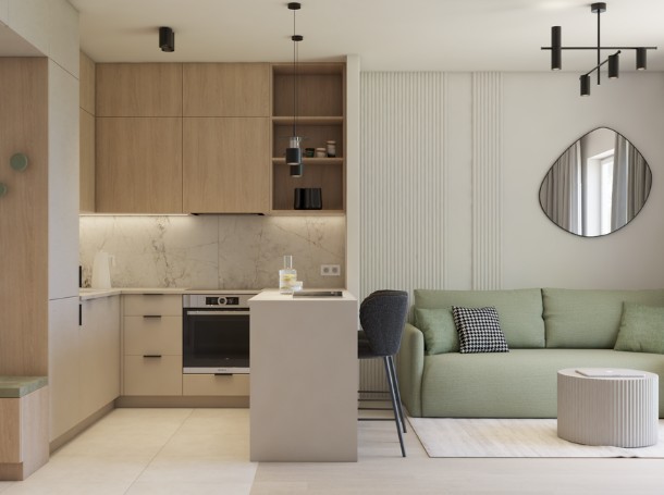 Nowoczesne mieszkanie z aneksem kuchennym z jasnego drewna i marmurowym wykończeniem, małą wyspą z hokerem oraz zieloną sofą i owalnym lustrem na ścianie.
