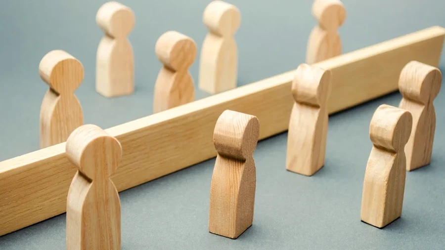 Wooden figurines facing each other on opposite sides of a wooden barrier.