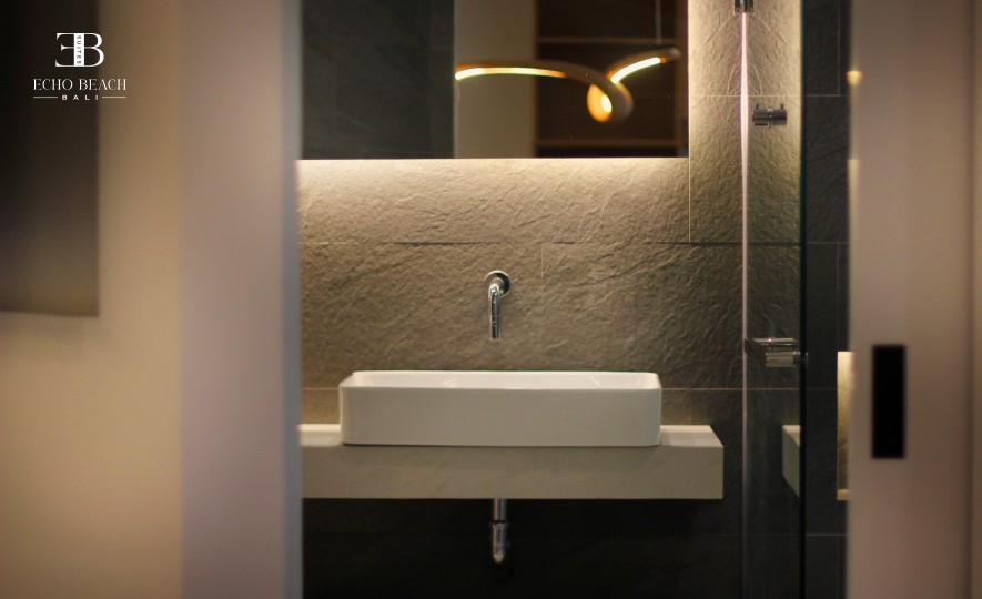 Close-up view of the modern stone bathroom vanity with a white vessel sink, wall-mounted faucet, and illuminated mirror at the Echo Beach Suite in Canggu, Bali.