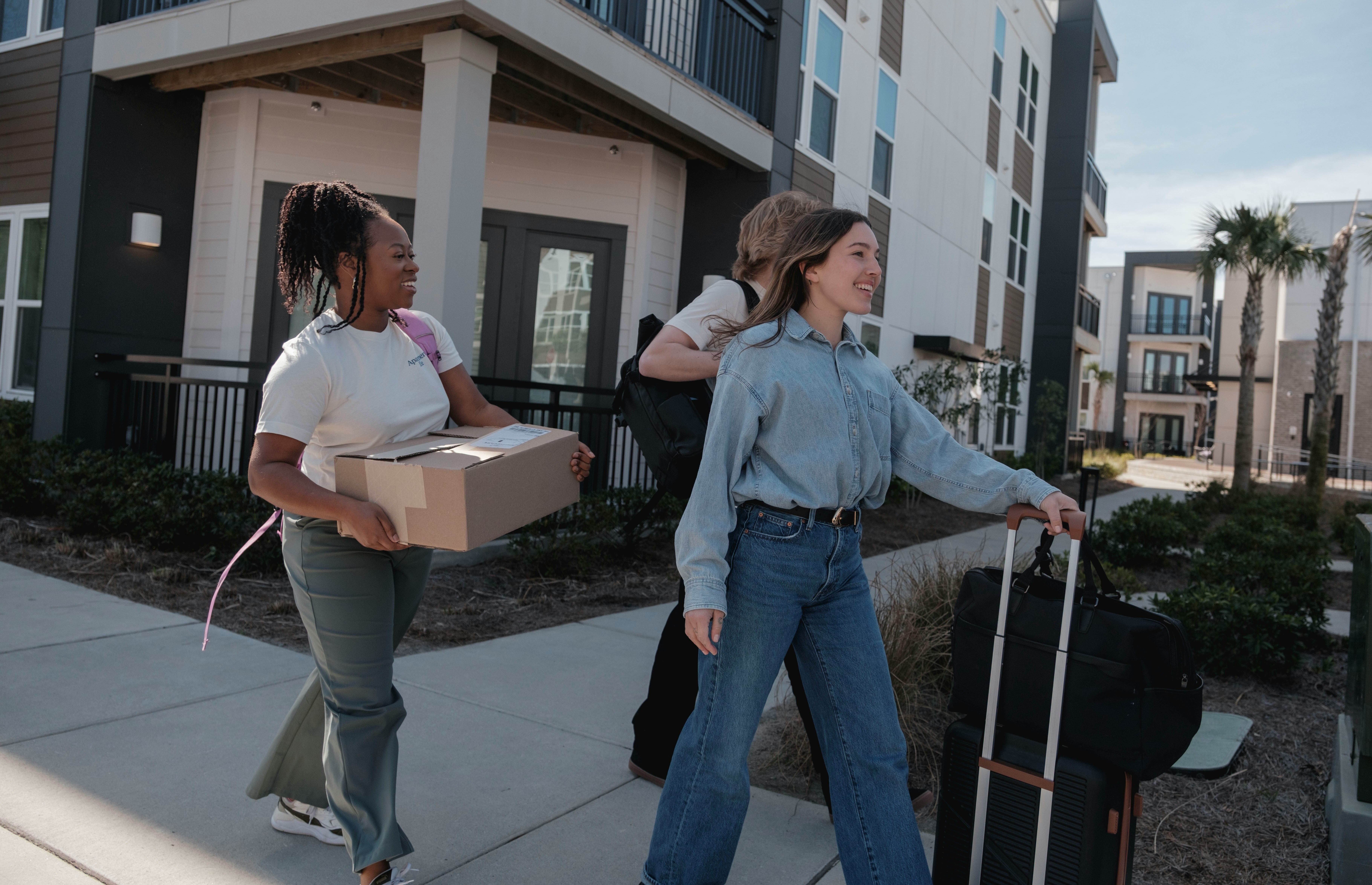 Two people carrying a box and a case out of an apartment building