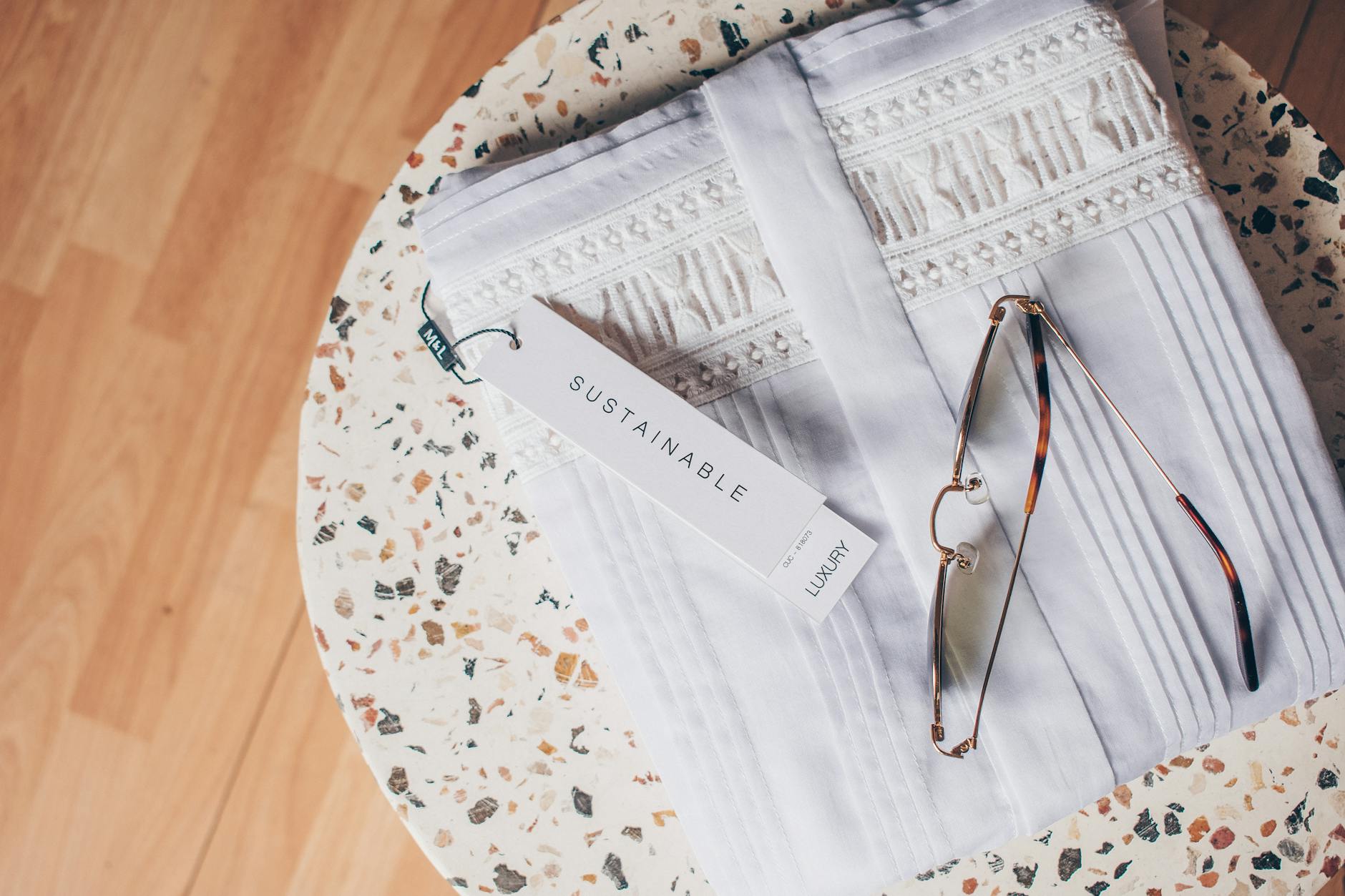 Folded white sustainable fabric with glasses on terrazzo coffee table, top view.