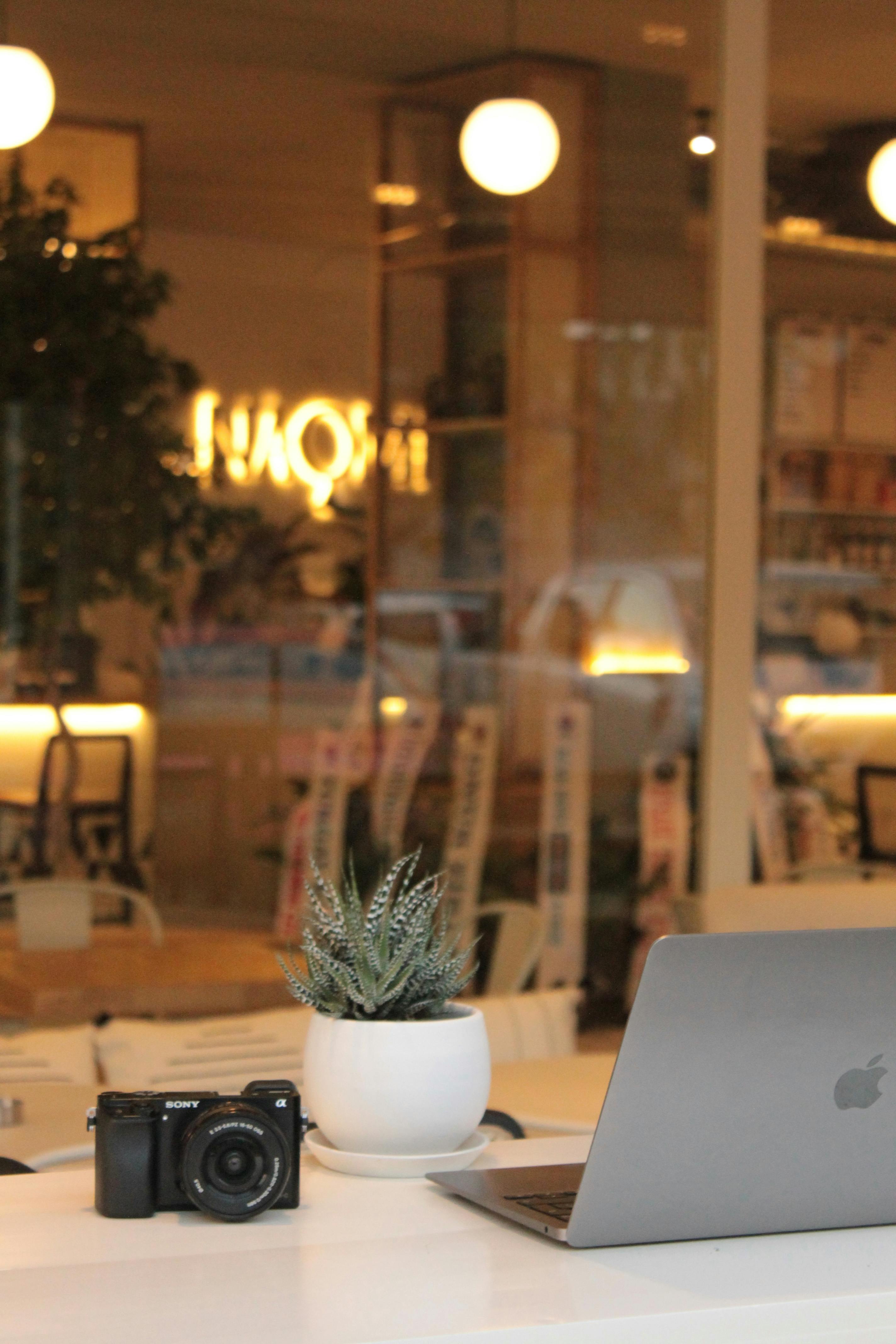 Kafedeki masanın üstündeki Macbook ve fotoğraf makinesi