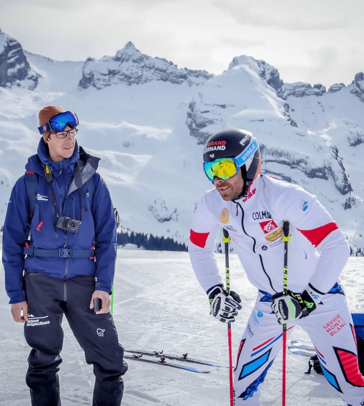 Hero Skieur professionnel en tenue Salomon discutant avec un membre de l’équipe Outdoor Perspectives sur une piste enneigée.