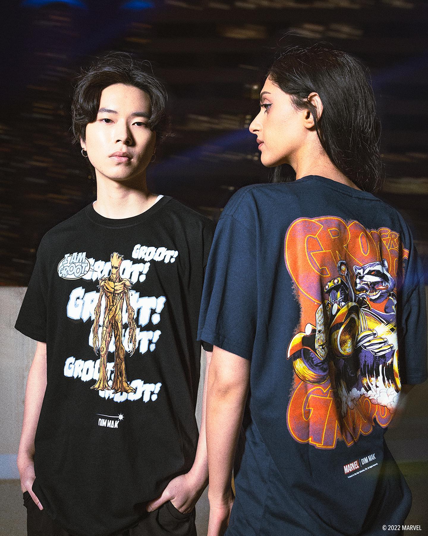 Two people stand back-to-back, wearing graphic t-shirts with distinct designs. One shirt features a colorful print.