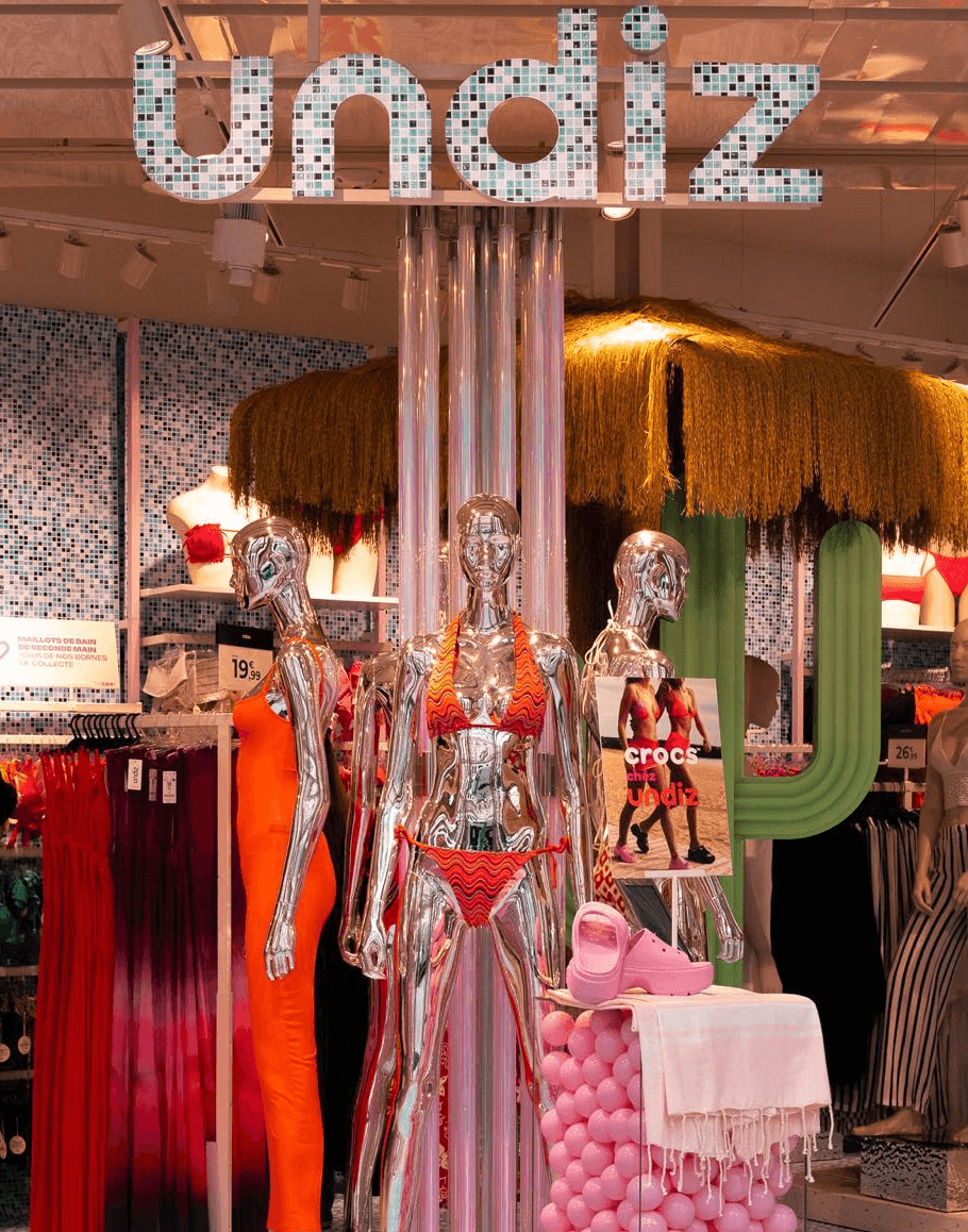 Intérieur de boutique Undiz avec mannequins chromés, maillots de bain, et décor tropical pour l’été 2024.
