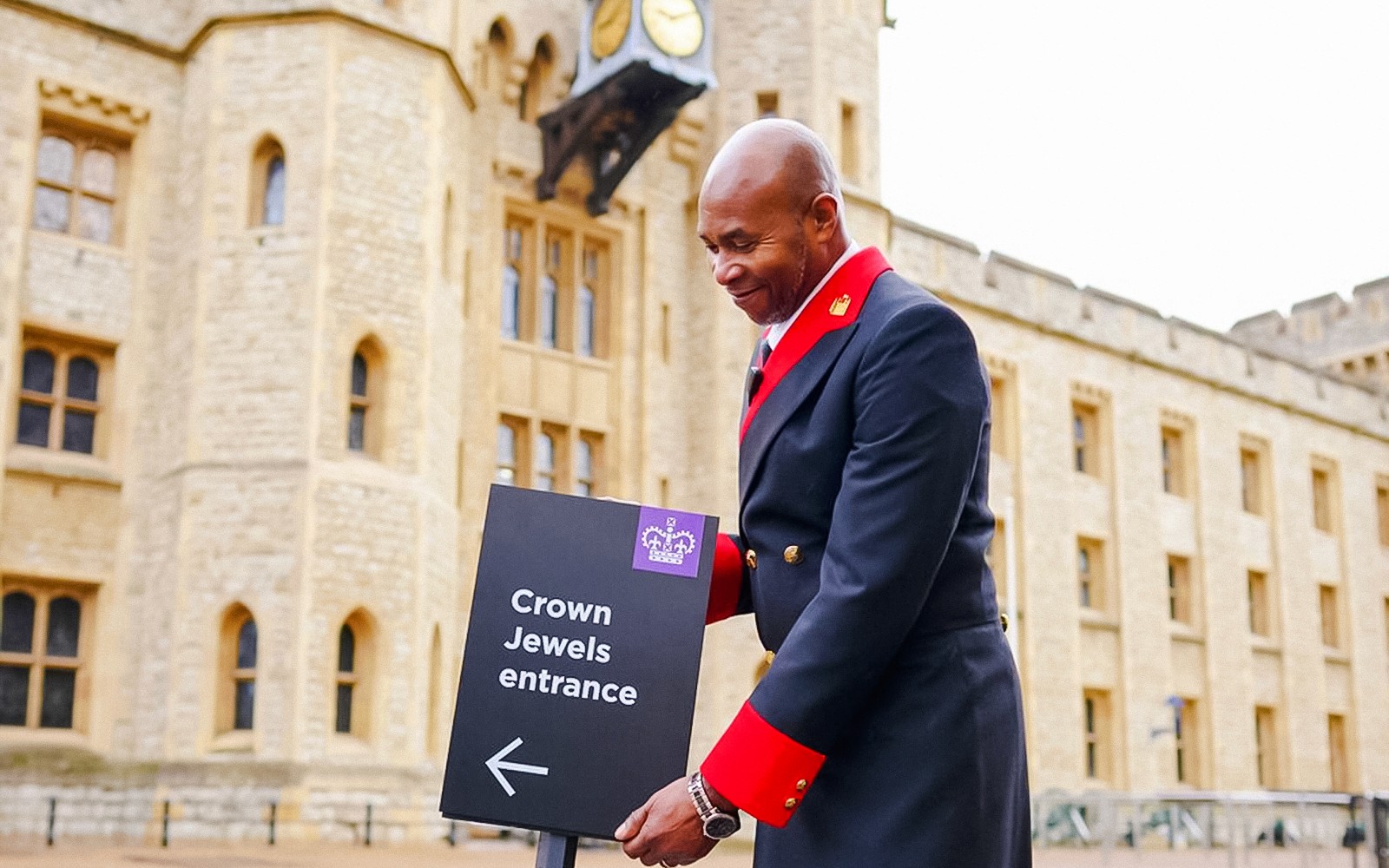 Вывеска входа к Королевским Драгоценностям в Лондонском Тауэре с рядом стоящим униформированным охранником.