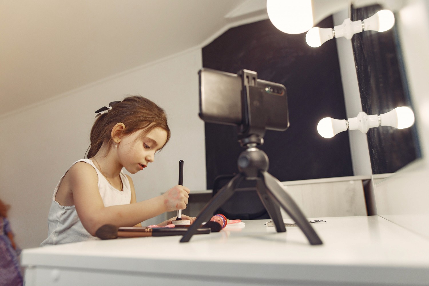 A young girl sits at a desk, focused on her camera, capturing moments with a look of curiosity and excitement.