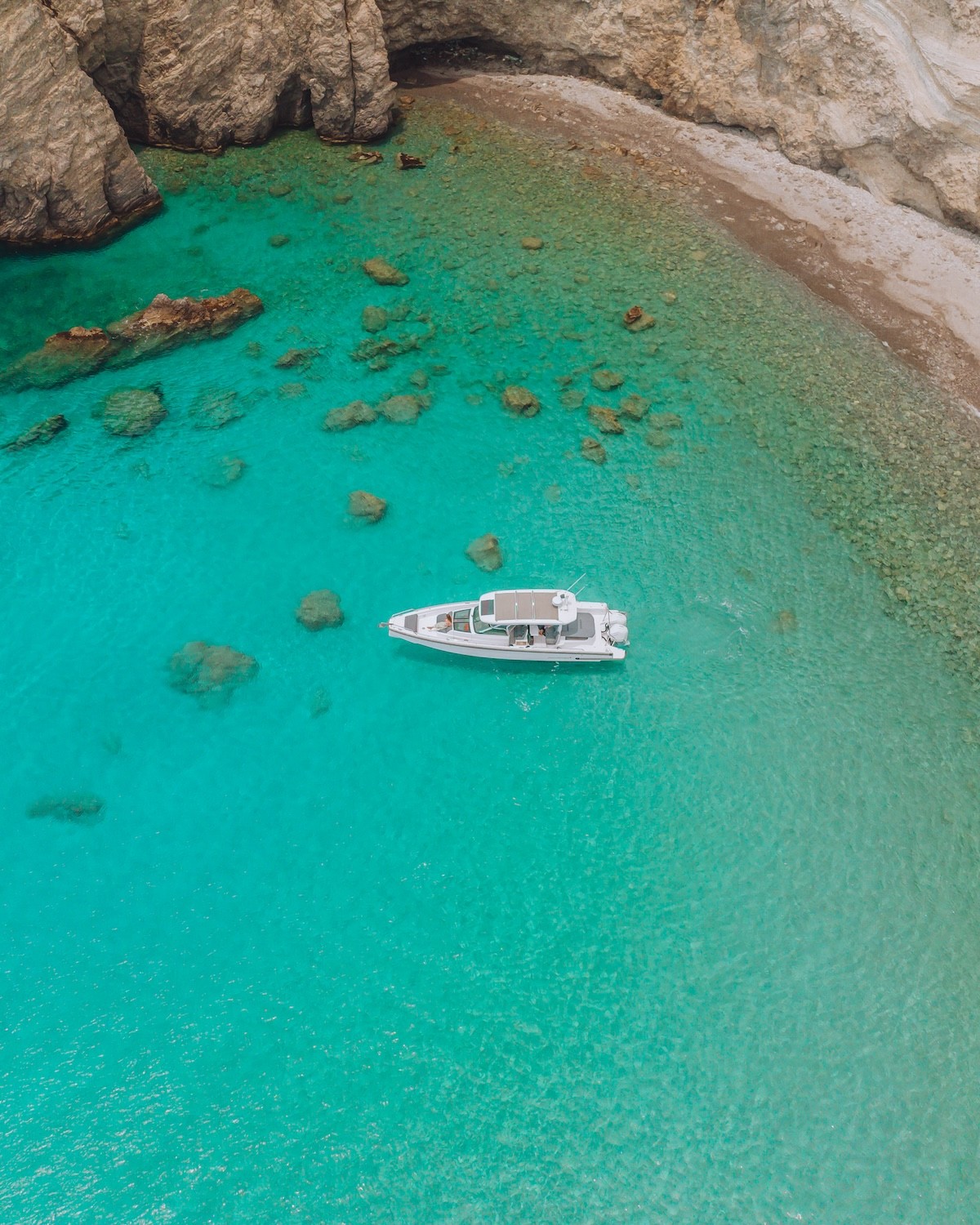Aerial view of white Axopar 37 motor yacht floating in crystal-clear turquoise waters with visible seabed below.